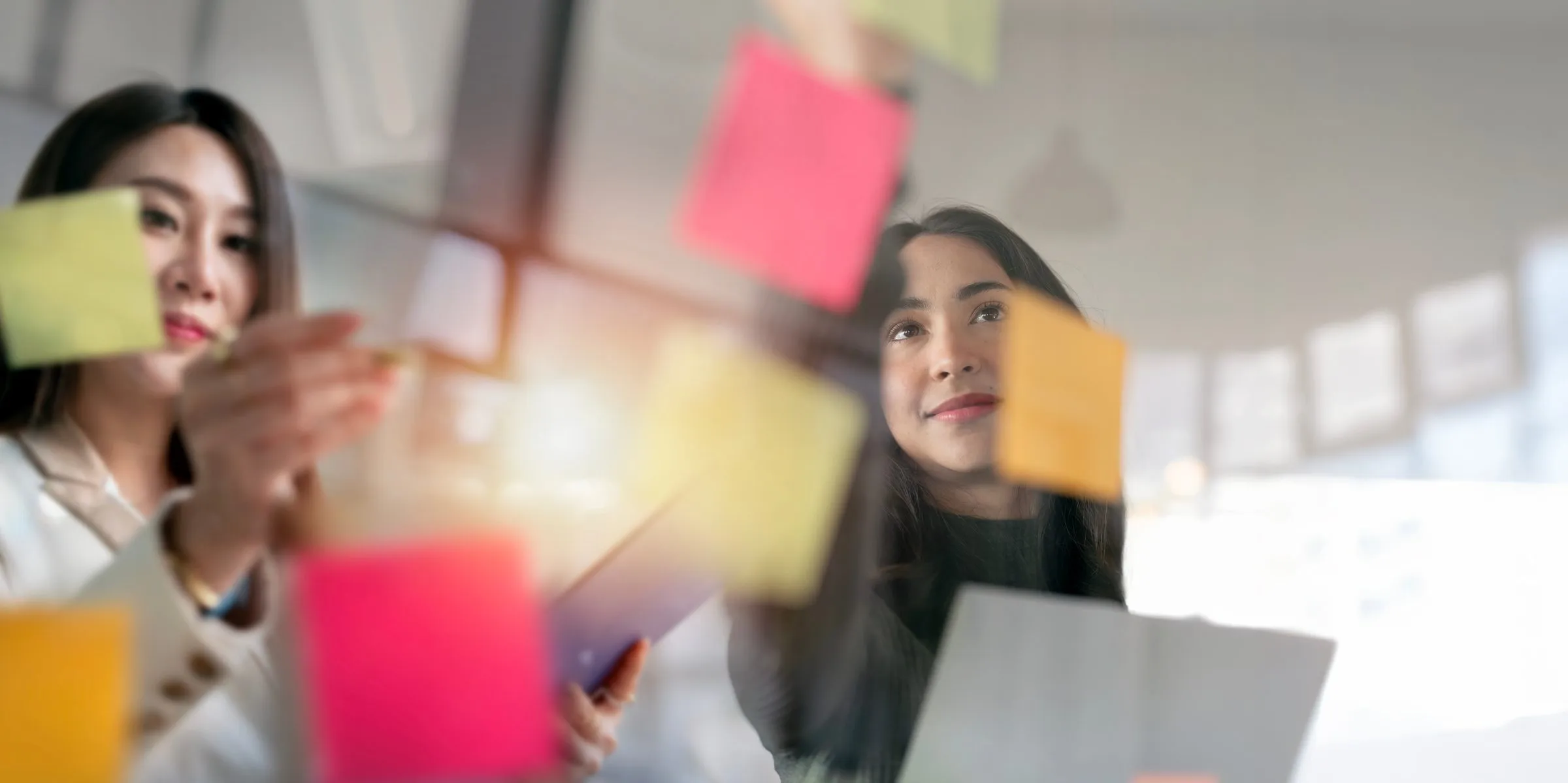 Two colleagues arranging coloured sticky notes on a glass wall