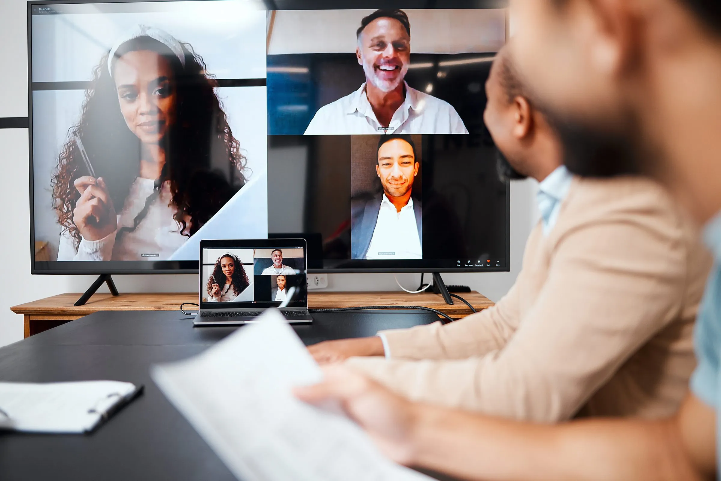 A person on a video call with four colleagues on screen in a meeting room
