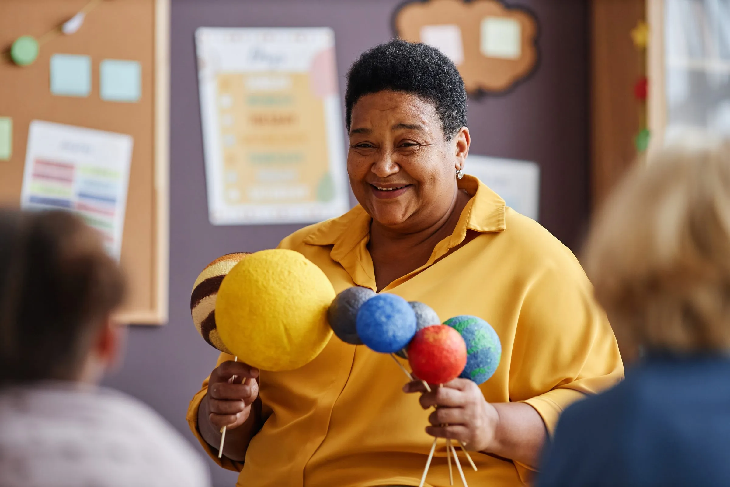 A teacher holding a handmade model of the planets in a decorated classroom