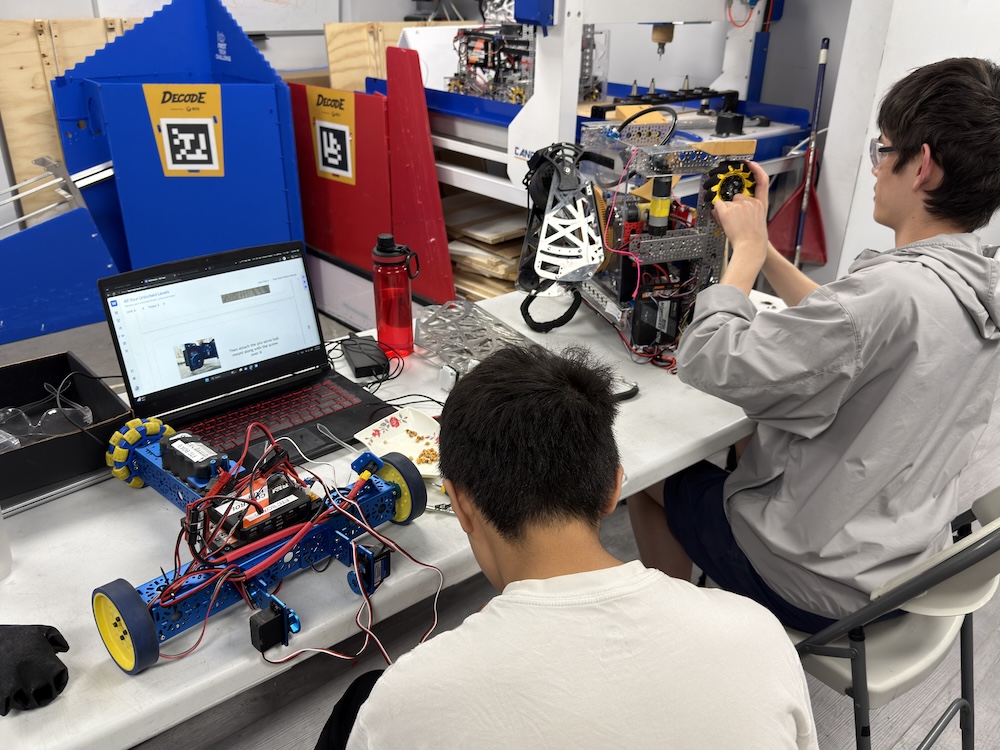High school students collaborating on assembling and programming an advanced competition robot in STEM camp.