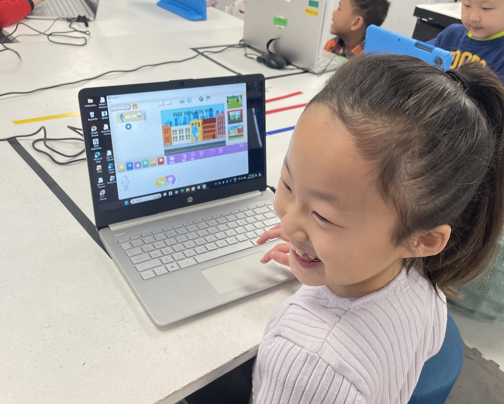 Student working on laptop designing 3D game worlds with Lua code in Roblox Studio class.