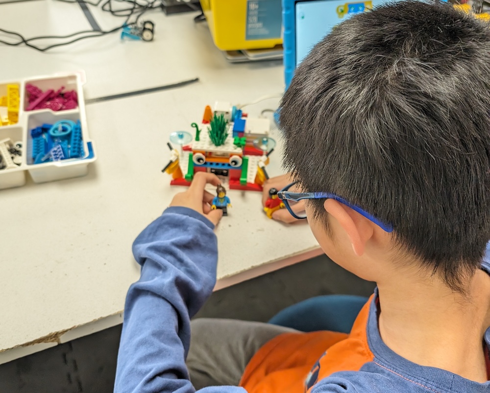 Young student assembling colorful gears on a LEGO SPIKE Essential robot for introductory coding.