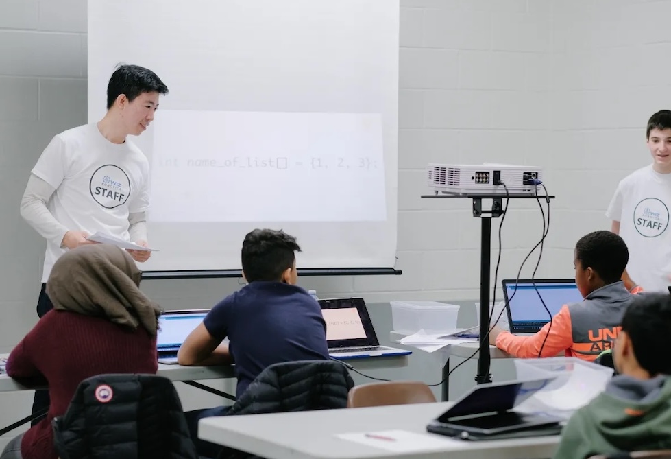 Youth student writing text-based Python code and algorithms on a laptop in coding class.