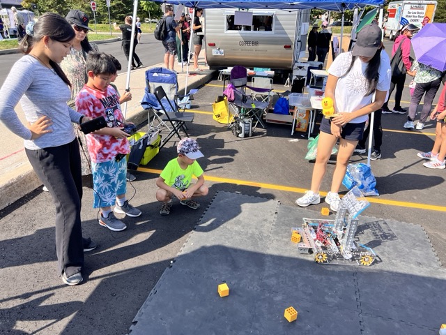 在 Wiz Robotics 户外社区活动展位上，青少年与儿童在导师指导下亲自操作金属竞赛机器人演示。