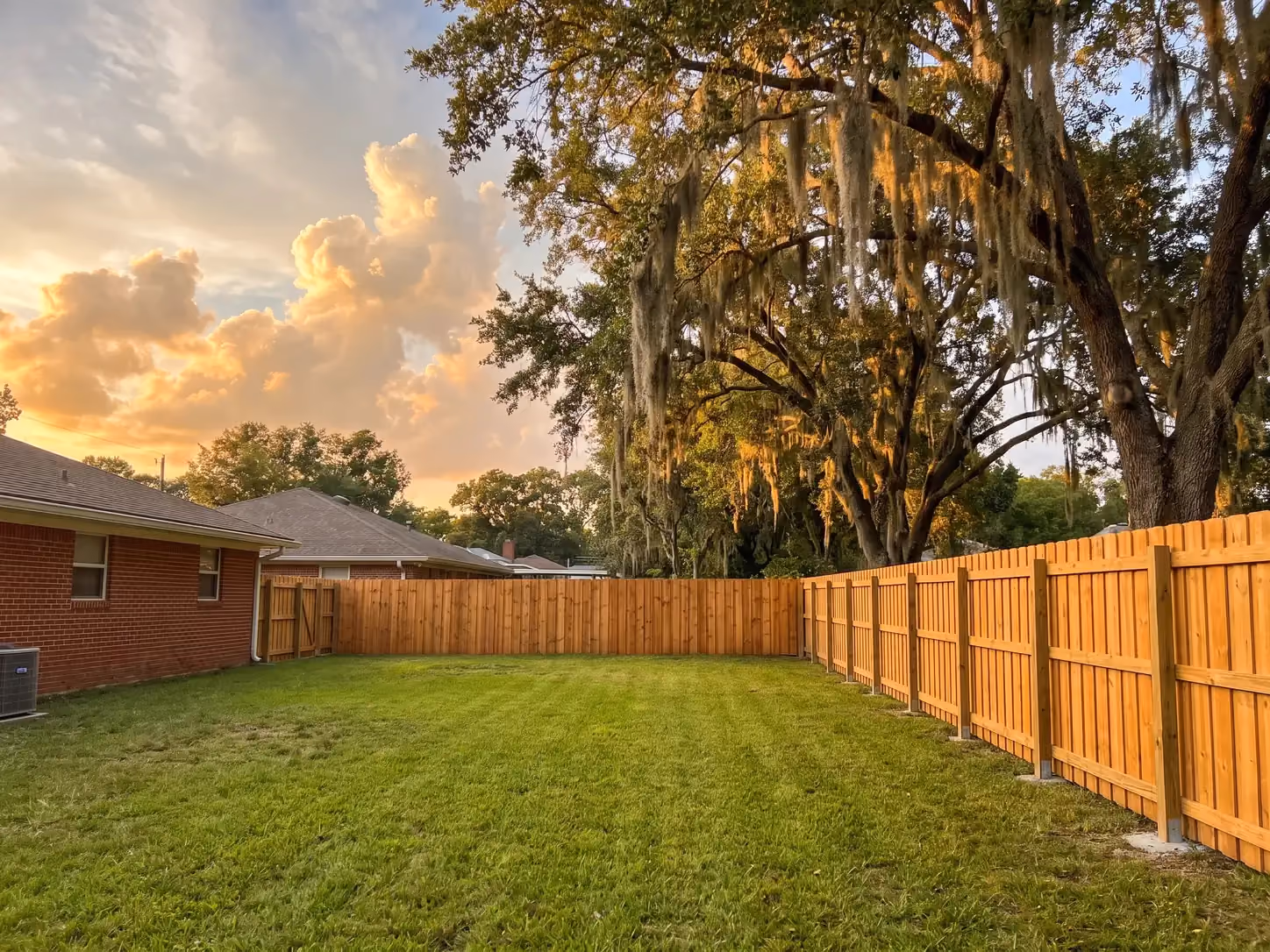 Cedar board-on-board privacy fence installed along a brick ranch home's backyard in Southeast Houston, TX at golden hour