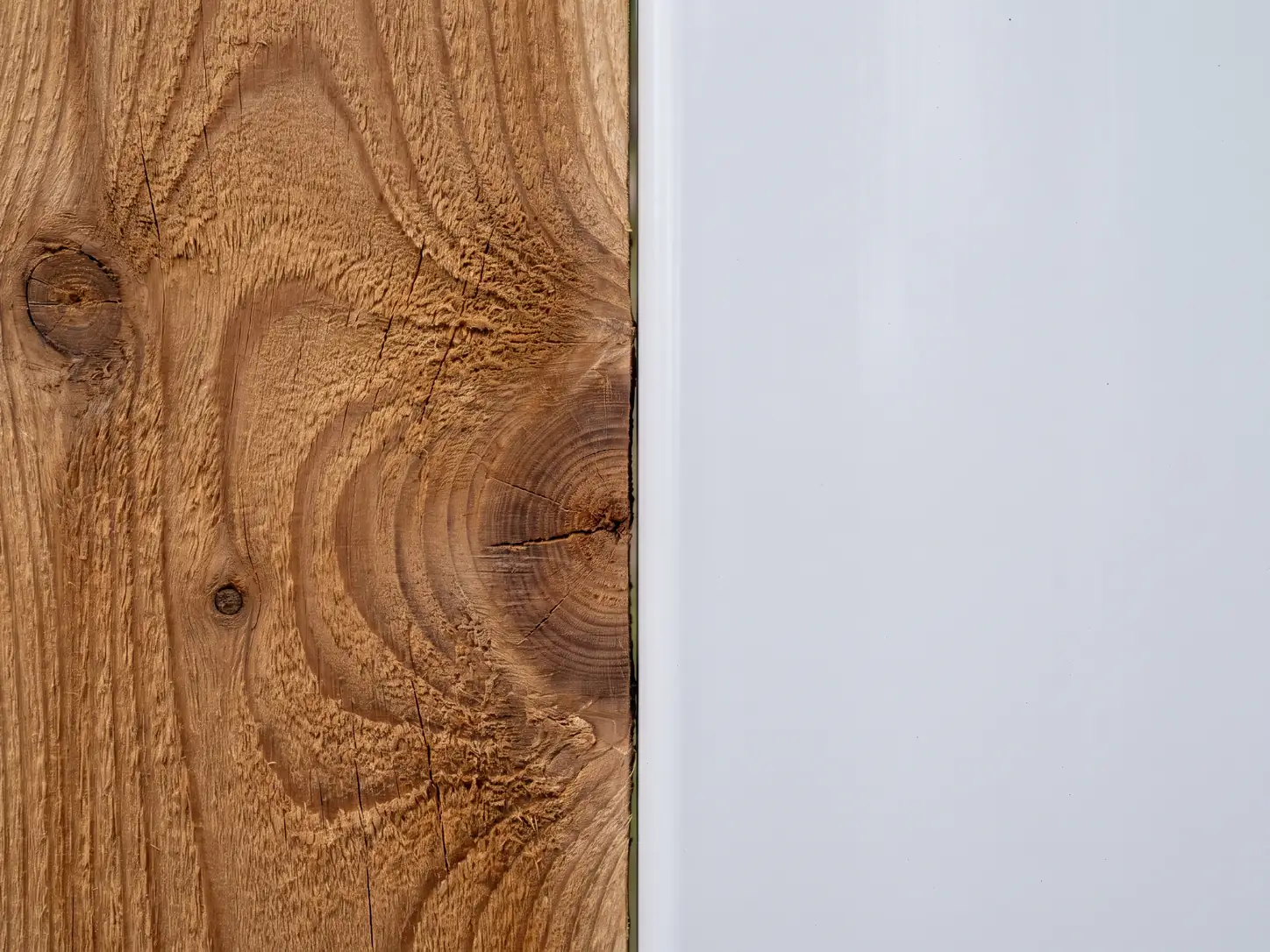 Close-up split of cedar wood grain beside a smooth white vinyl fence surface