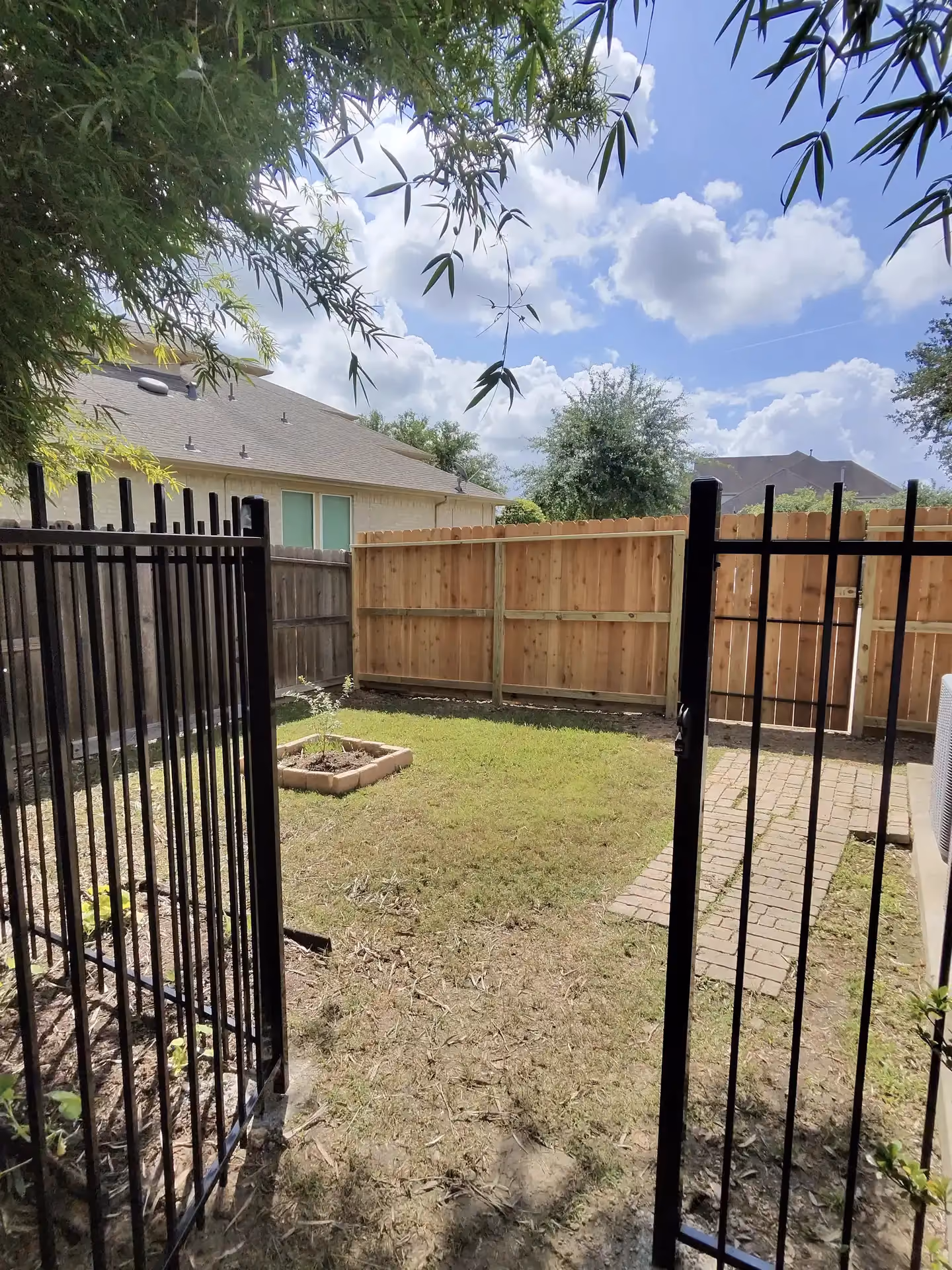 A new cedar privacy fence meets a black wrought iron gate to enclose a backyard patio area on the Texas Gulf Coast.