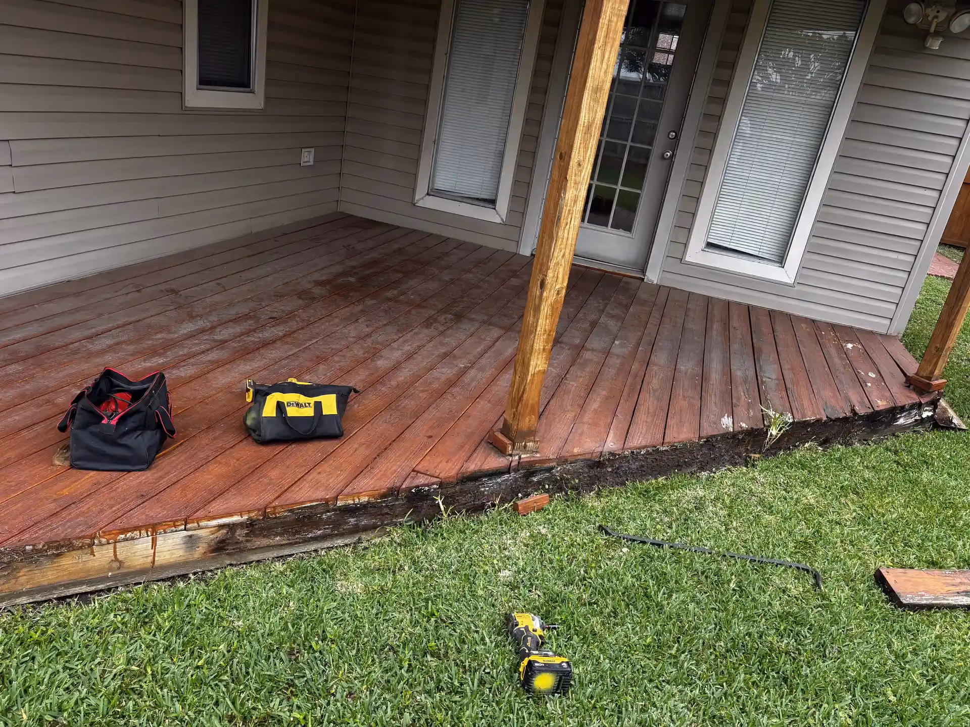 A reddish-brown stained wood deck with a support post and two contractor tool bags resting on the boards in Houston, TX.