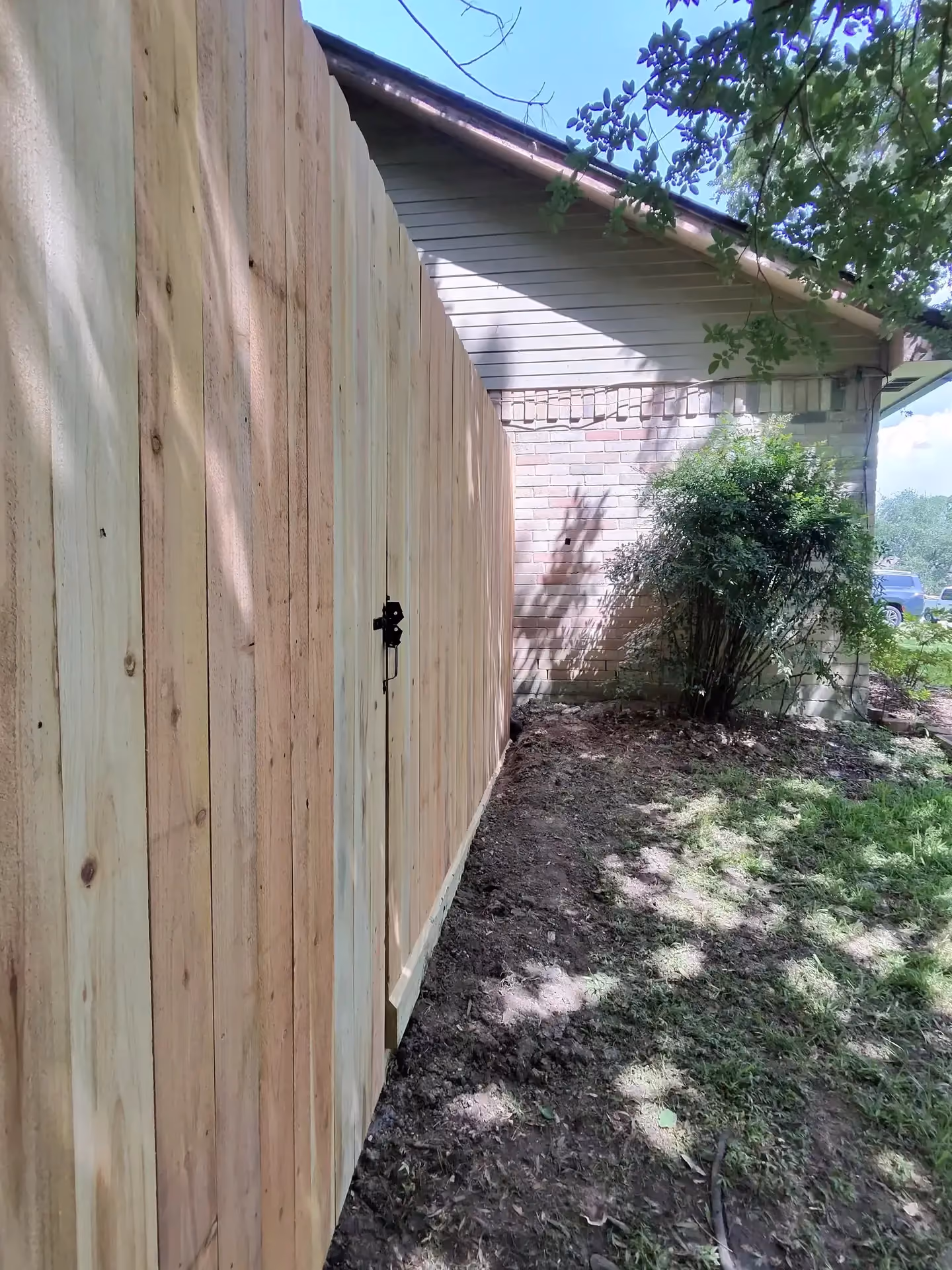 A freshly built light cedar privacy fence with a matching gate and black hardware beside a brick house in Houston, TX.