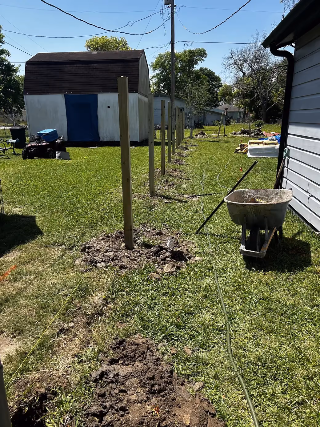 A line of freshly set wood fence posts stretching across a backyard toward a storage shed in Houston, TX.