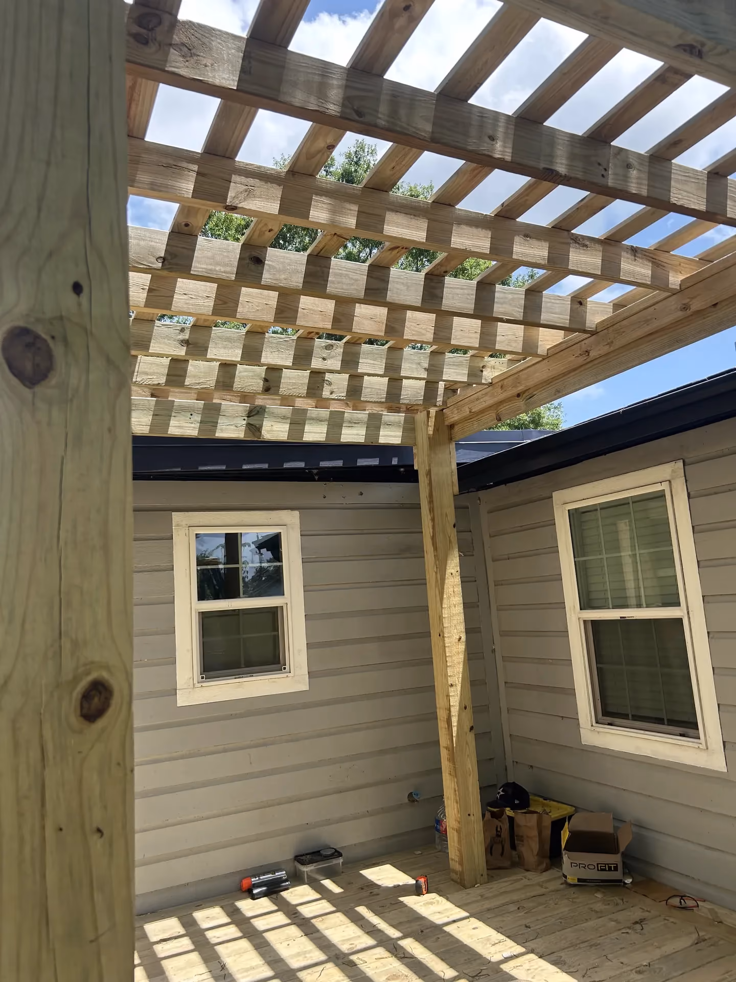 A cedar pergola with evenly spaced slatted rafters being built over a patio attached to a house in Houston, TX.