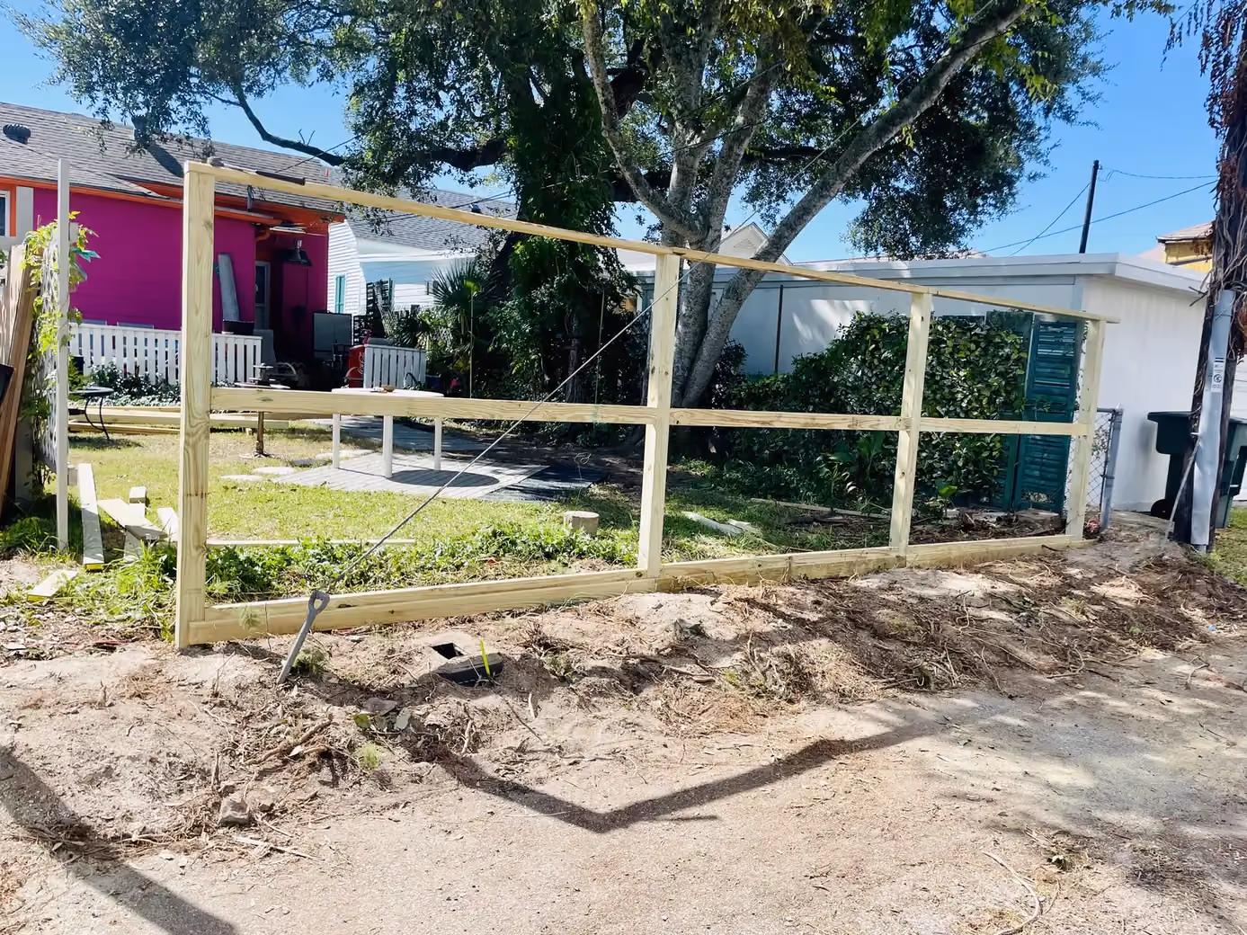 A large wood gate frame with cross bracing takes shape in a side yard near colorful houses in Houston, TX.