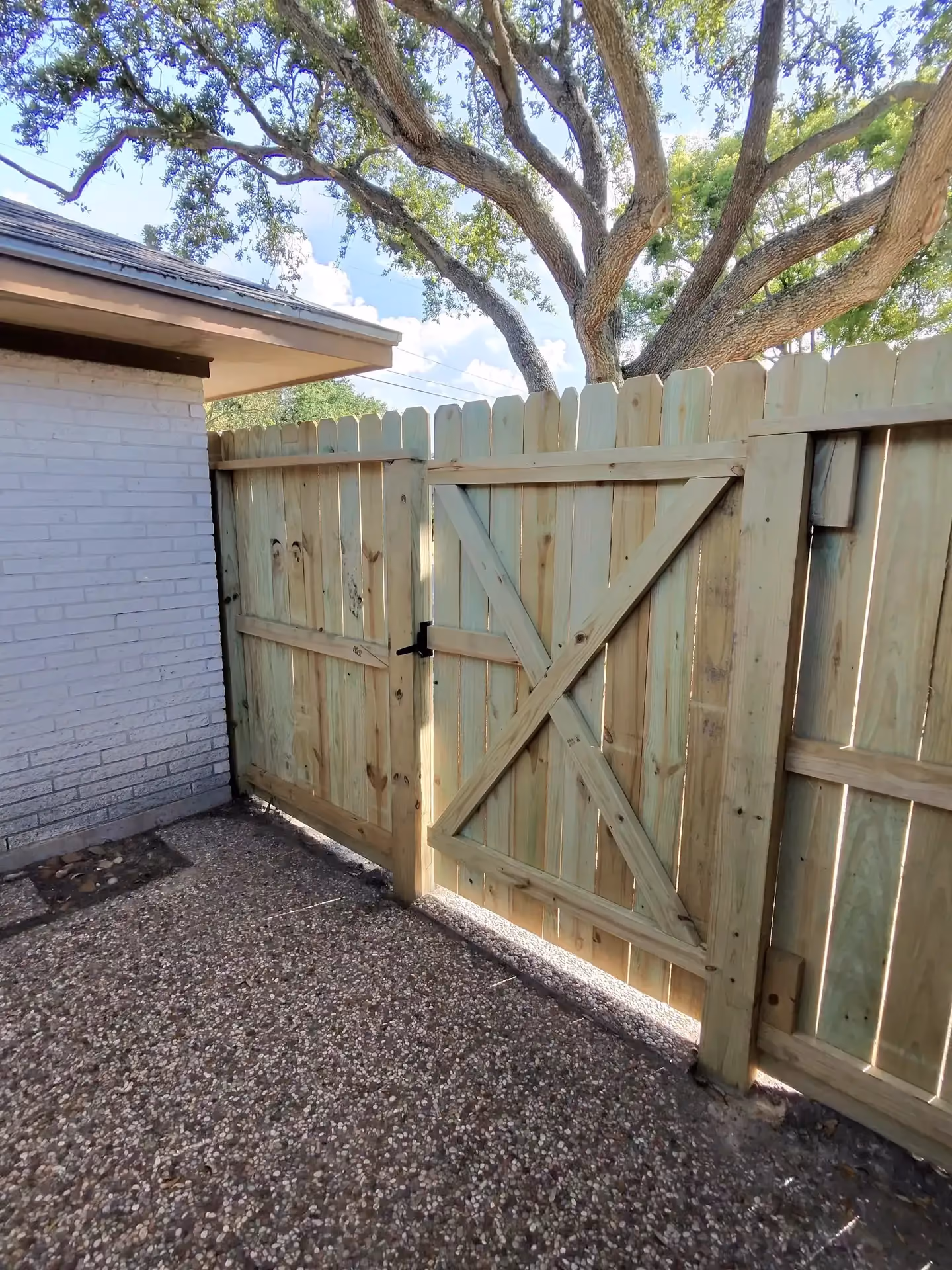 A new wood picket gate featuring a diagonal X-brace and black latch beside a white brick house in Houston, TX.