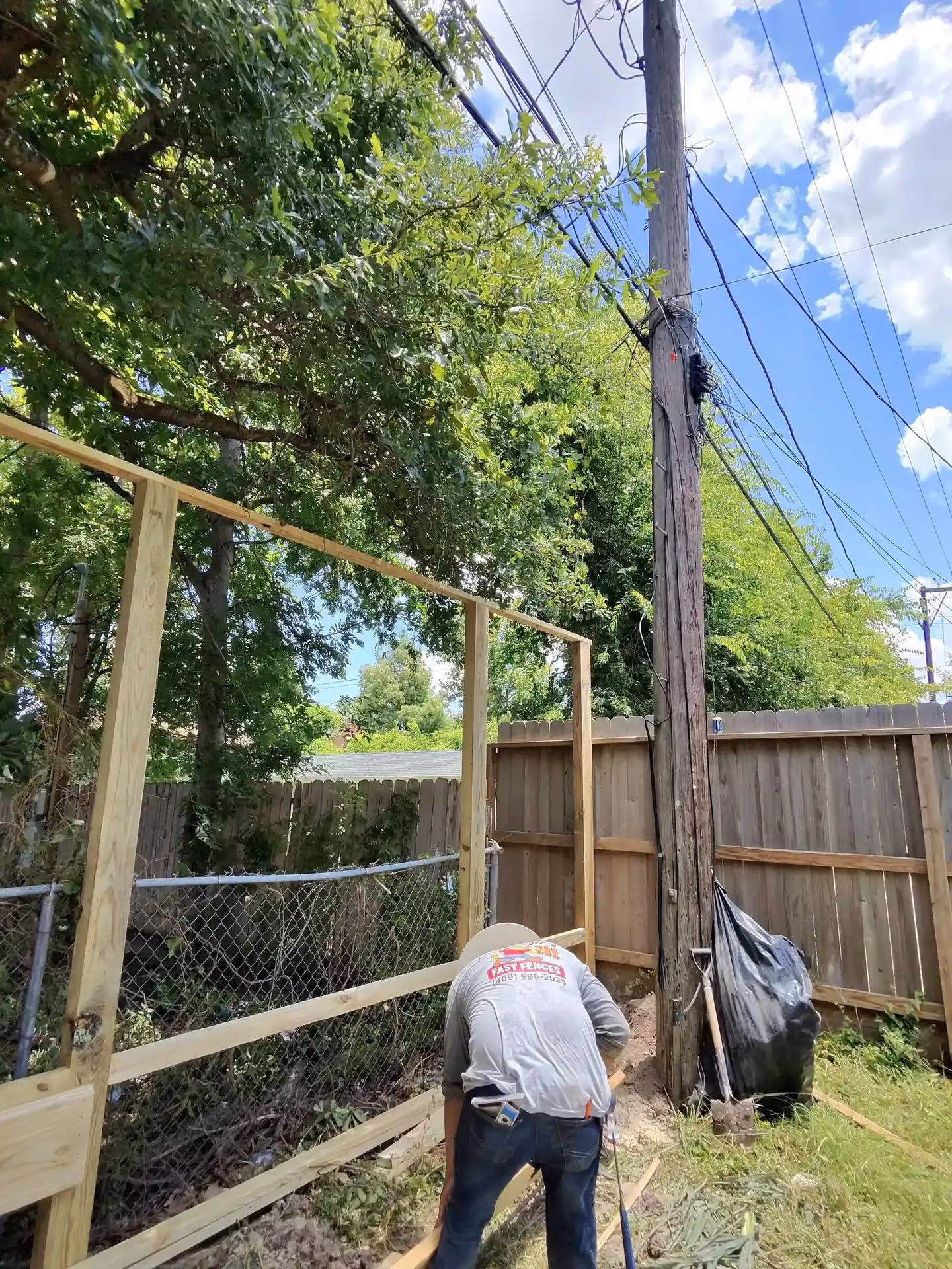 A Fast Fences crew member in a branded shirt assembling wood fence framing next to a utility pole and chain link in Houston, TX.