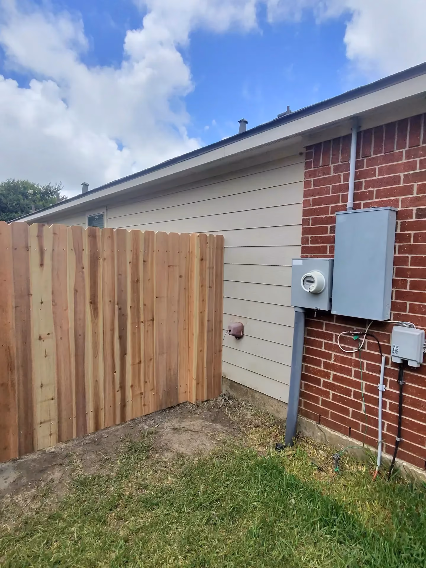 A newly built cedar privacy fence forms a clean corner beside a white board-and-batten home in Pearland, TX.