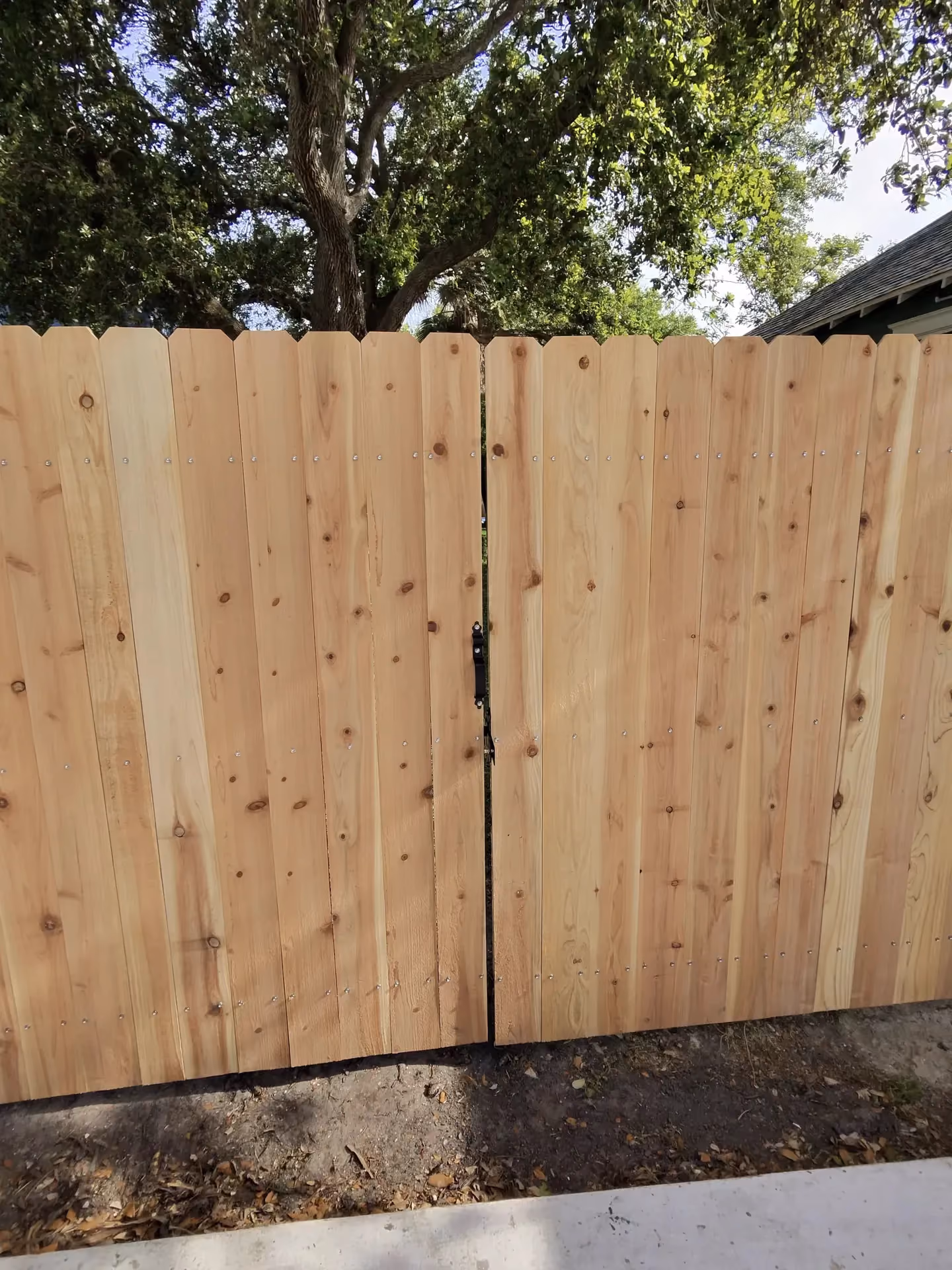 A pair of matching unstained cedar gates with a center latch spans a driveway entrance in Pearland, TX.