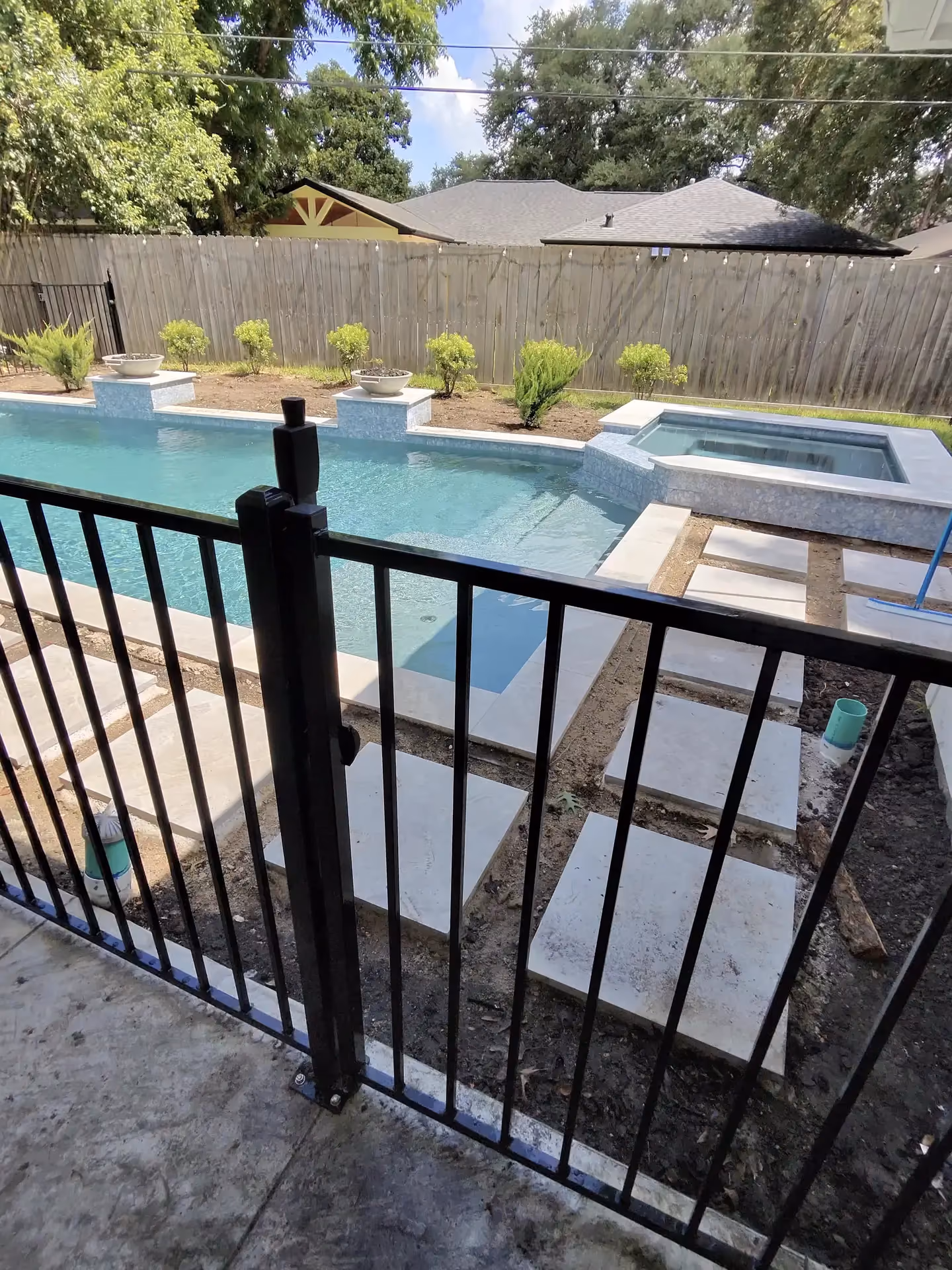 A black aluminum fence borders a newly tiled pool patio with travertine pavers on the Texas Gulf Coast.