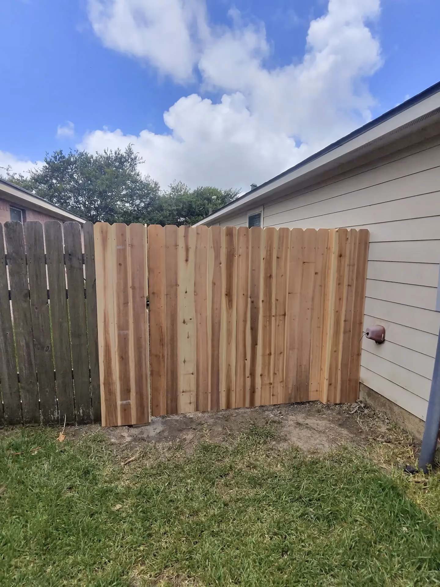 A new cedar dog-ear fence and gate tie into a beige house corner on the Texas Gulf Coast.