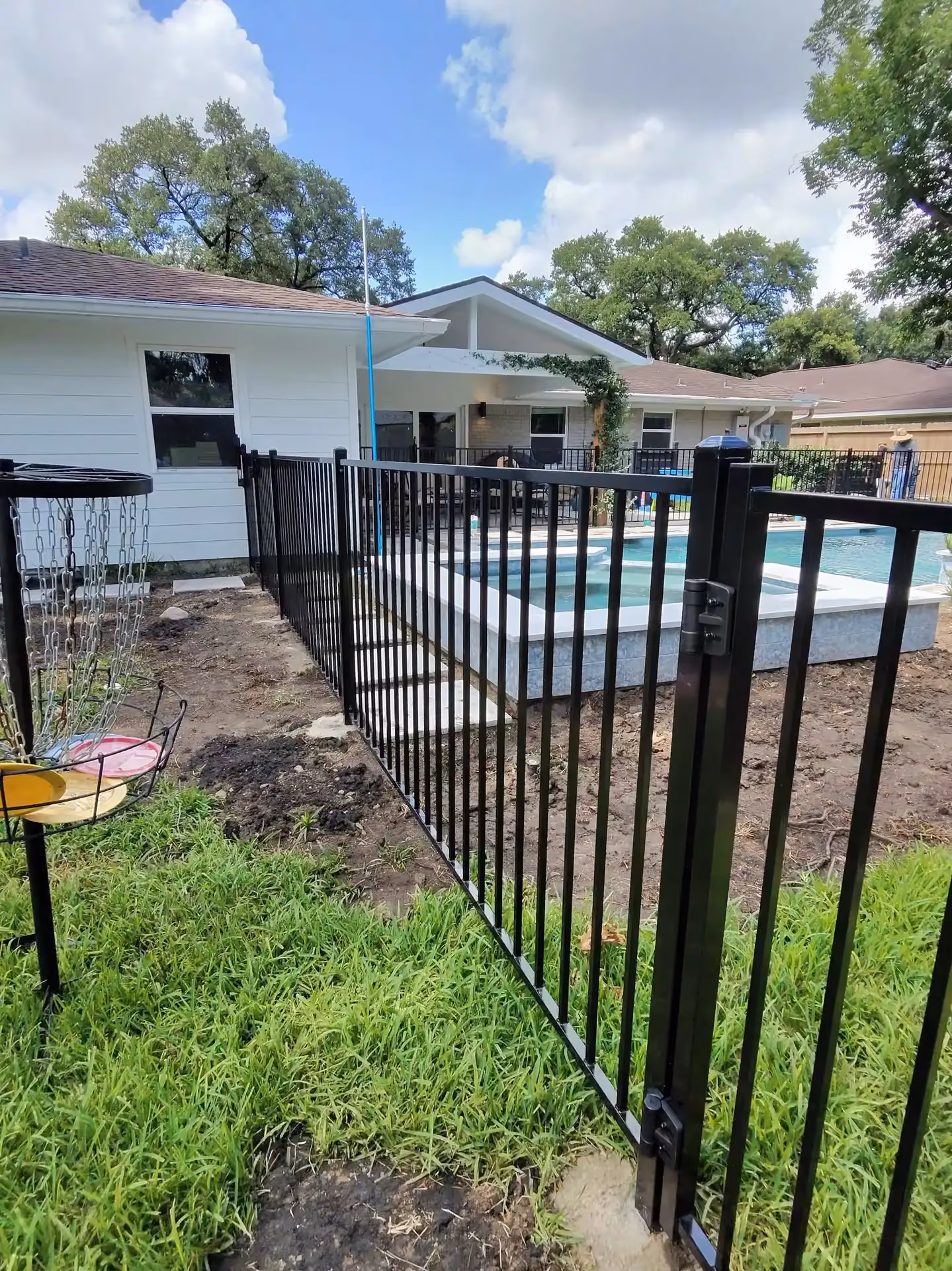 A black aluminum fence encloses a backyard pool and spa near a white gabled home on the Texas Gulf Coast.