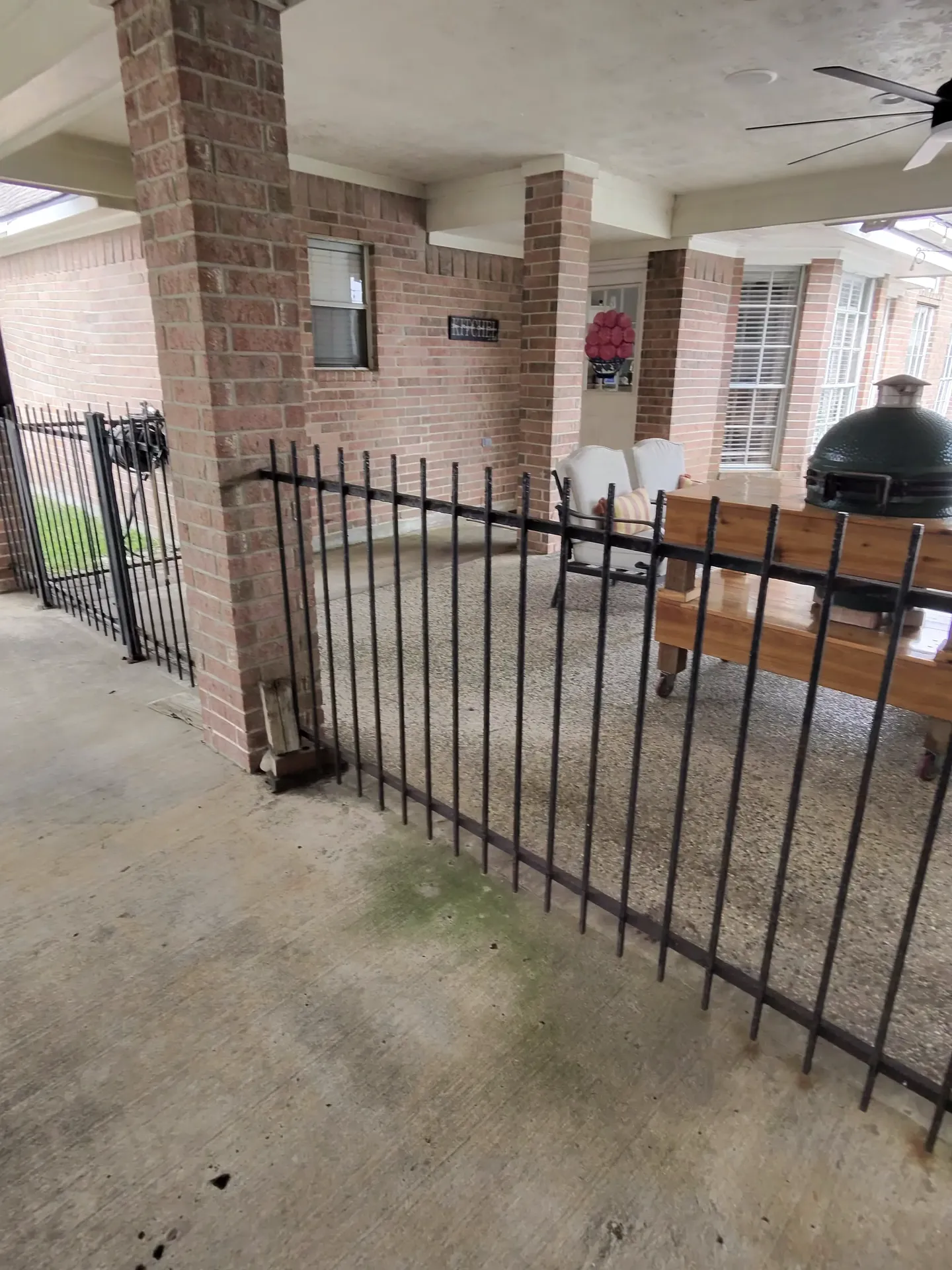 A black wrought iron fence encloses a brick-columned patio with outdoor seating and a grill in Friendswood, TX.