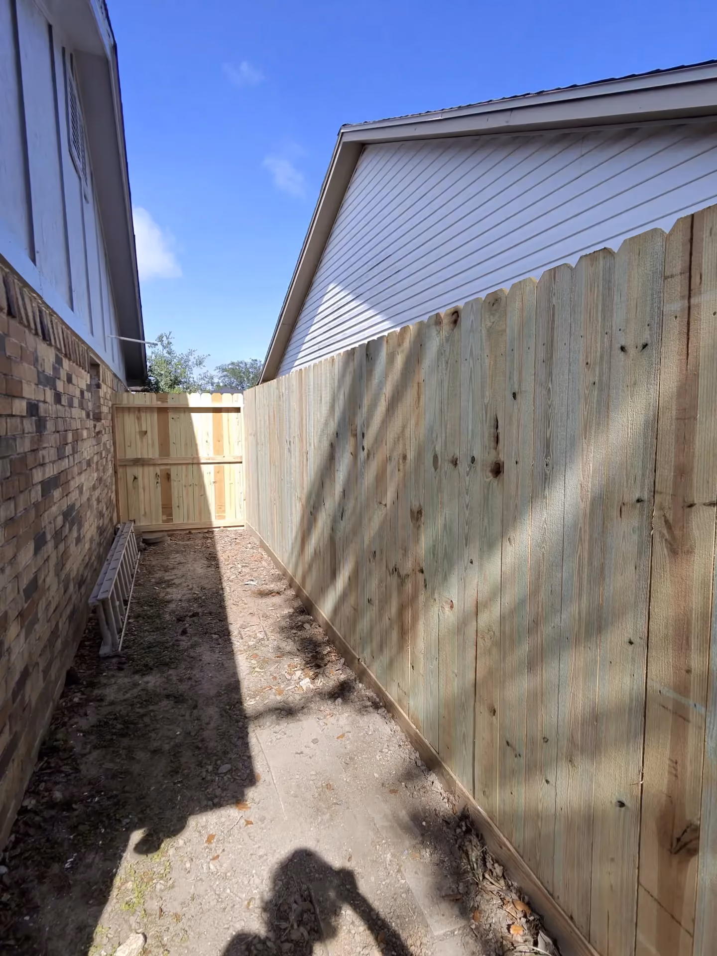 A new wood privacy fence lines a narrow side yard leading to a gate between two homes in Houston, TX.