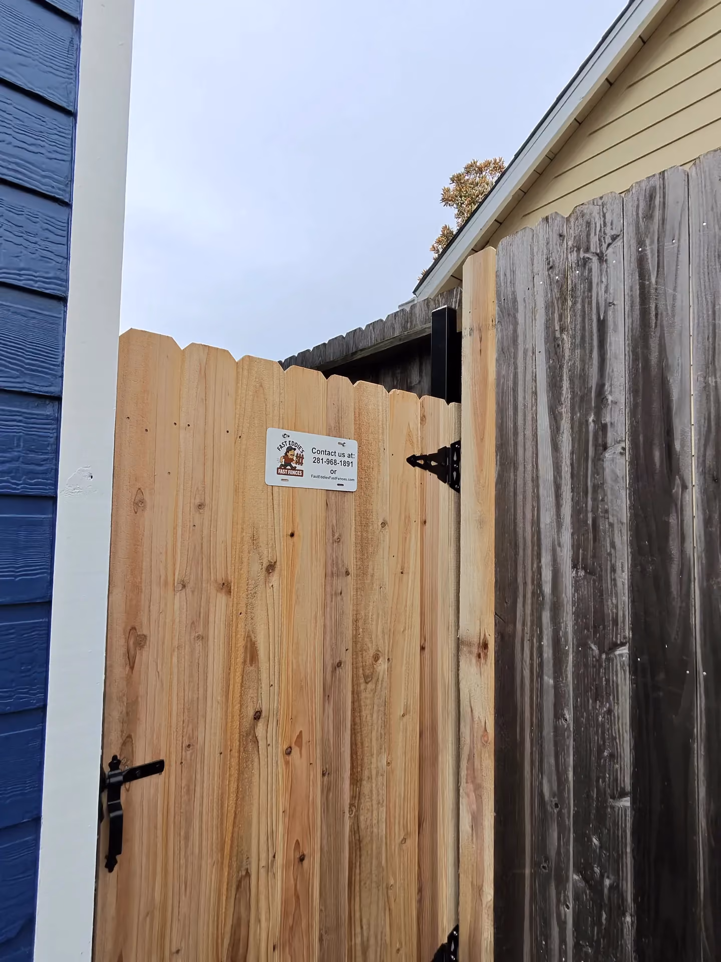 A new cedar wood gate with a Fast Eddie's Fast Fences tag stands beside a weathered fence in Houston, TX.
