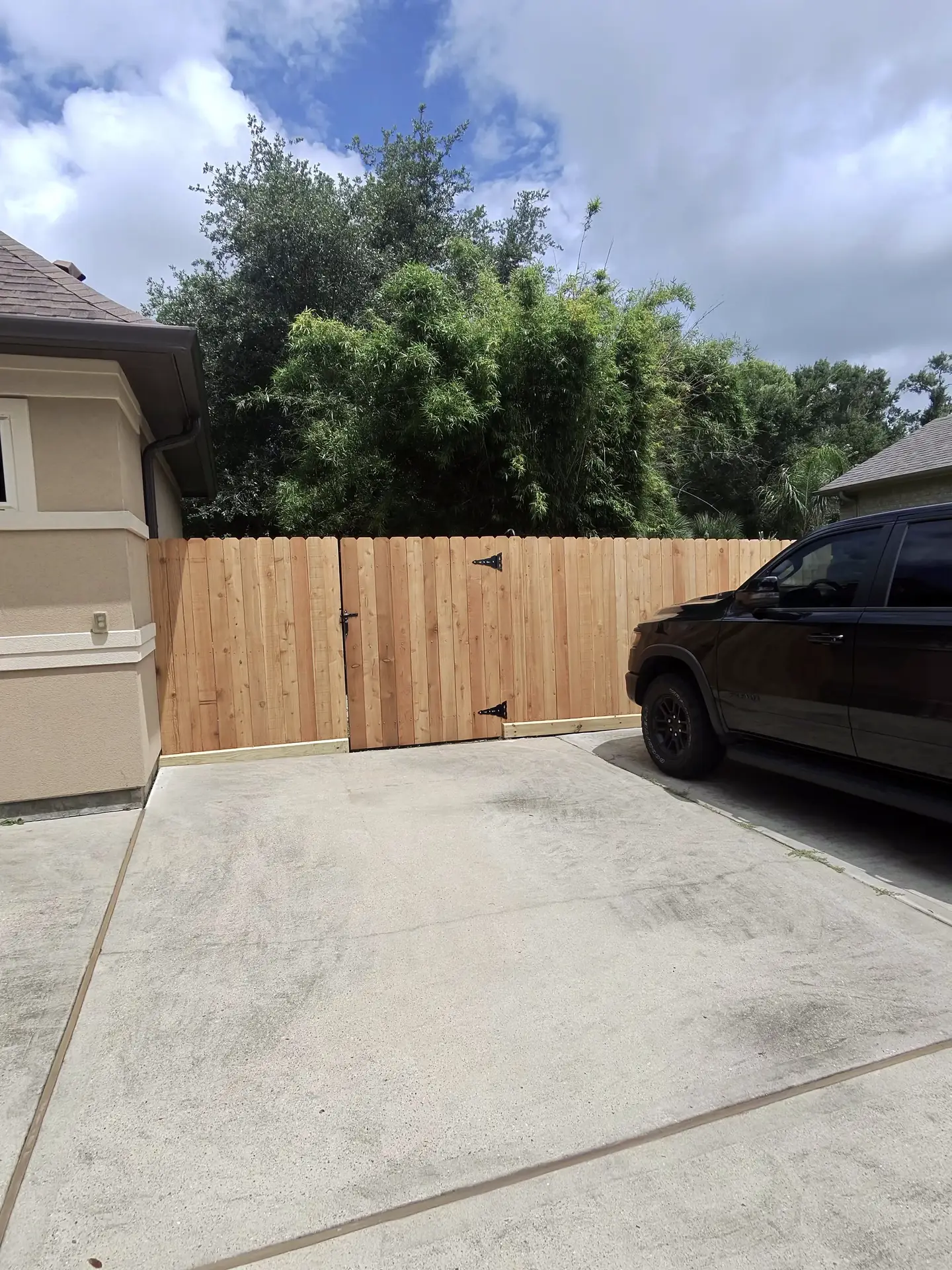 A finished cedar wood gate with black strap hinges secures a driveway beside a stucco home in Houston, TX.