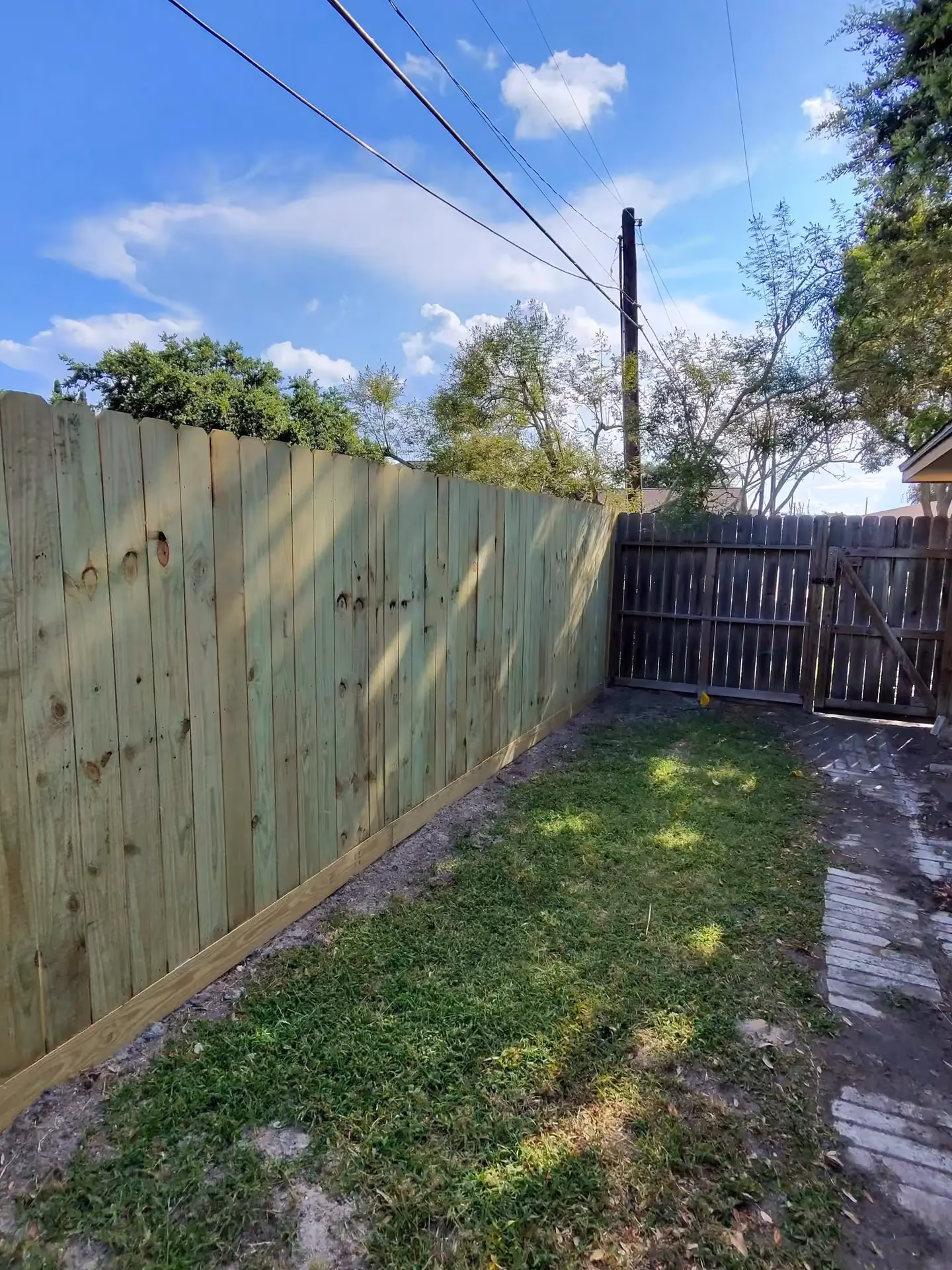 A new cedar wood fence section joins an older stained wood fence and gate in a backyard in Houston, TX.