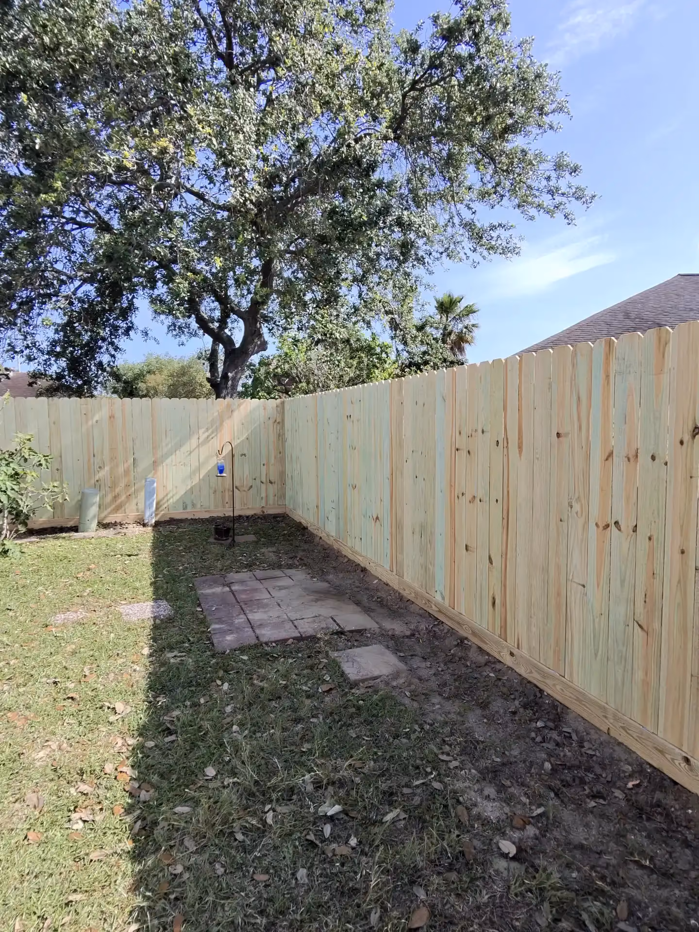 A new wood privacy fence turns the corner of a backyard patio with pavers and a lantern in Houston, TX.