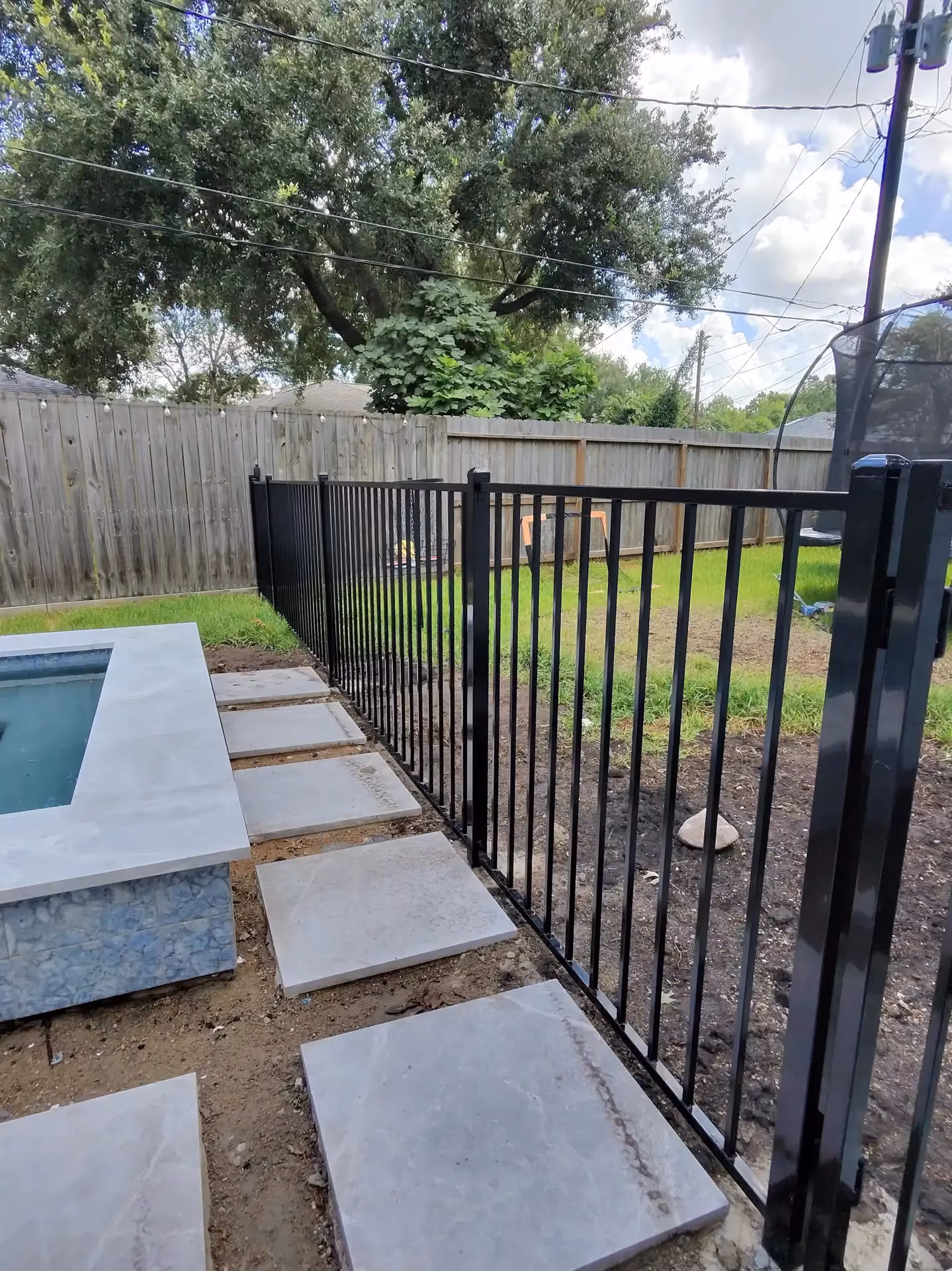 A black aluminum fence lines a pool patio with gray stone pavers and a raised spa in Houston, TX.