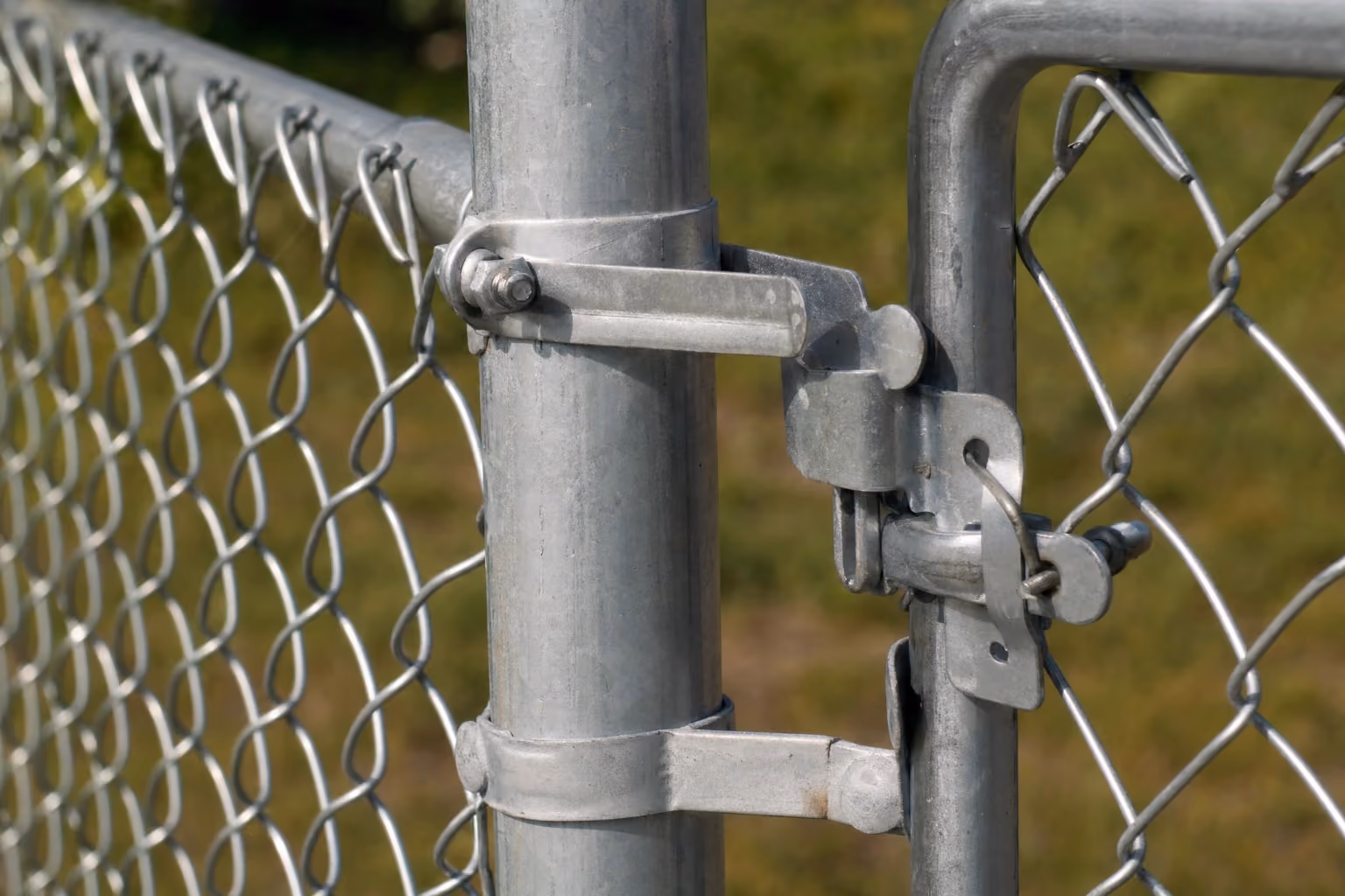Close-up of galvanized chain link mesh, tension band and gate latch hardware