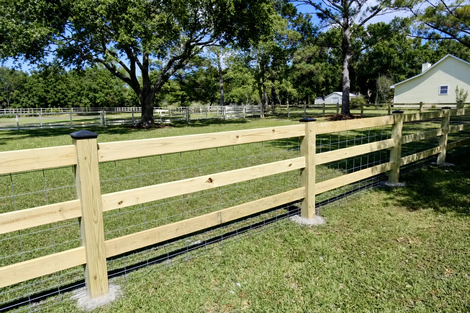 New 3-rail wooden farm and ranch fence with wire mesh on a green pasture near Houston, TX