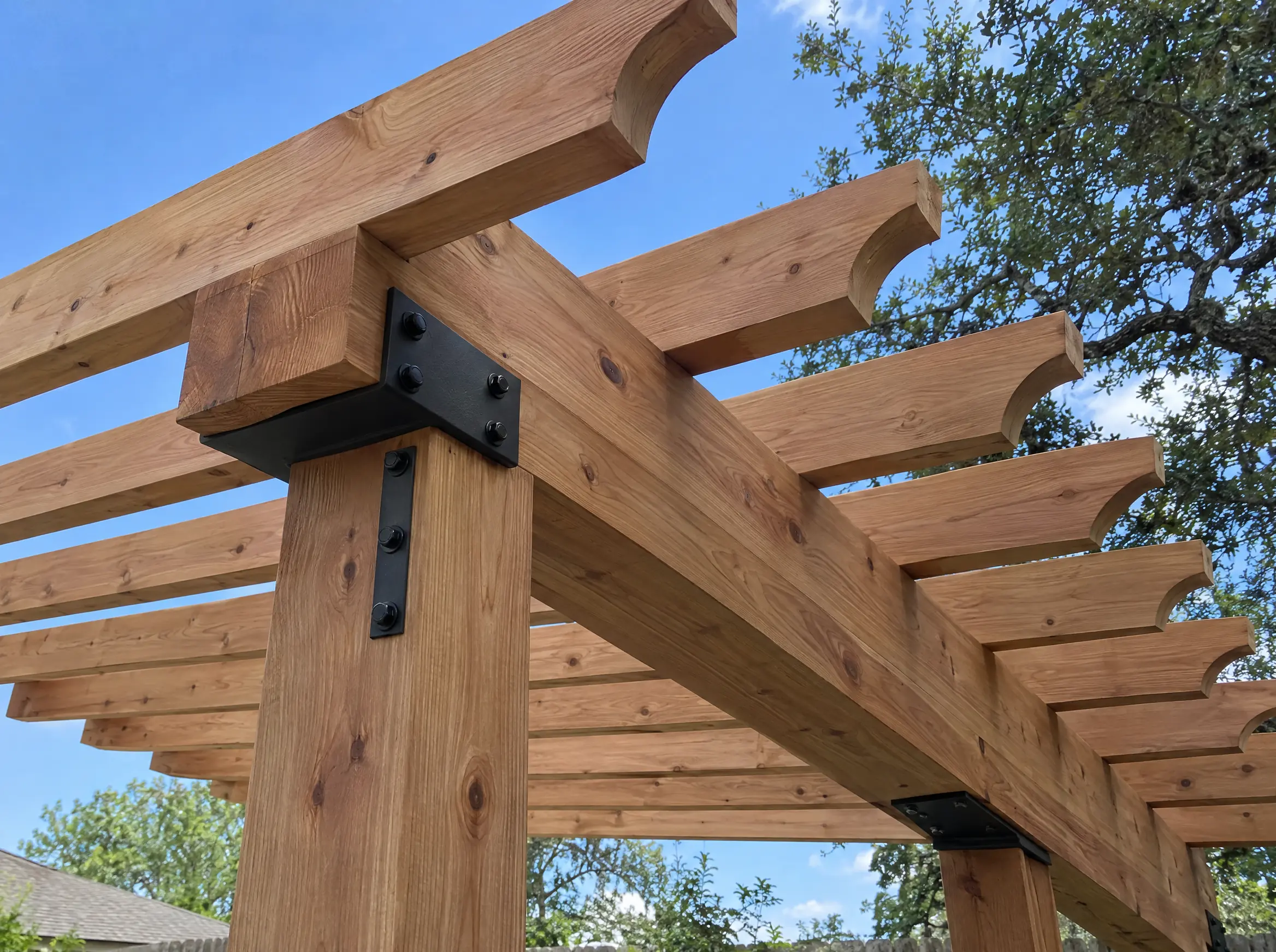 Close-up of a cedar pergola post, beam, and shaped rafter tails joined with black steel brackets