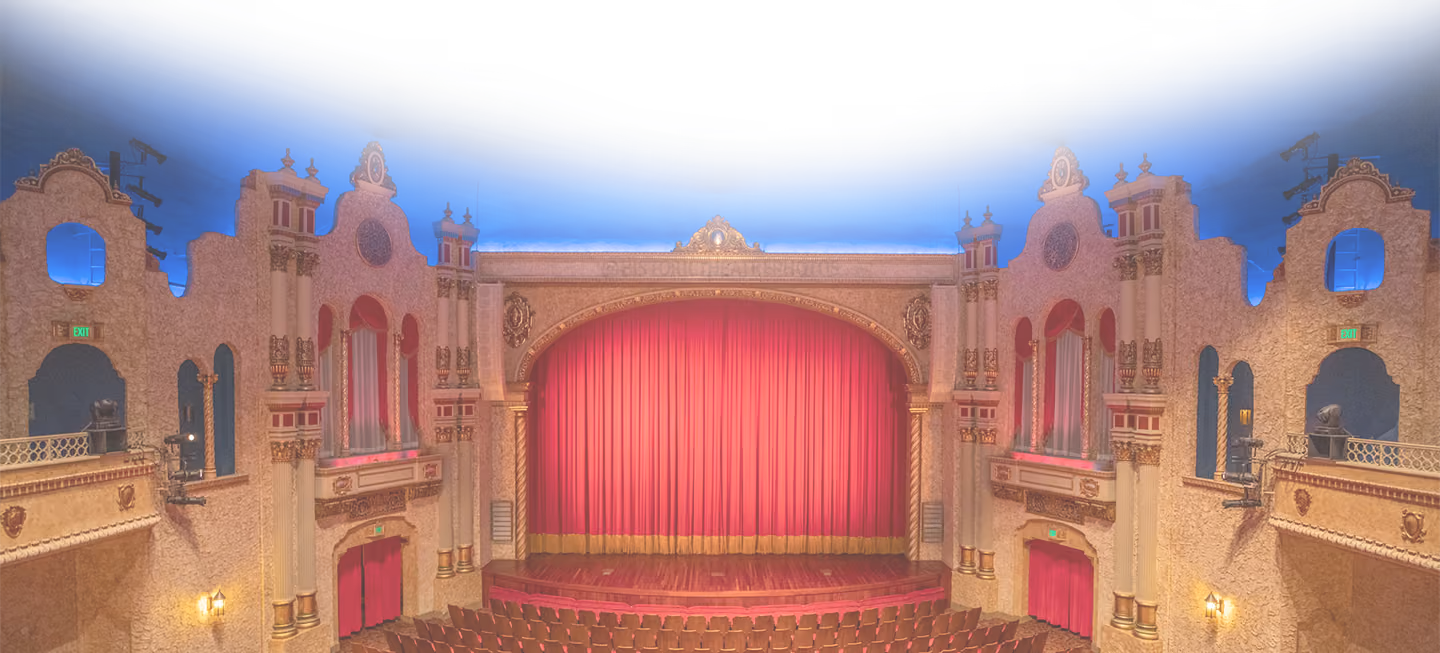 Ornate theater interior with red curtains, gold decorations, and a blue ceiling.
