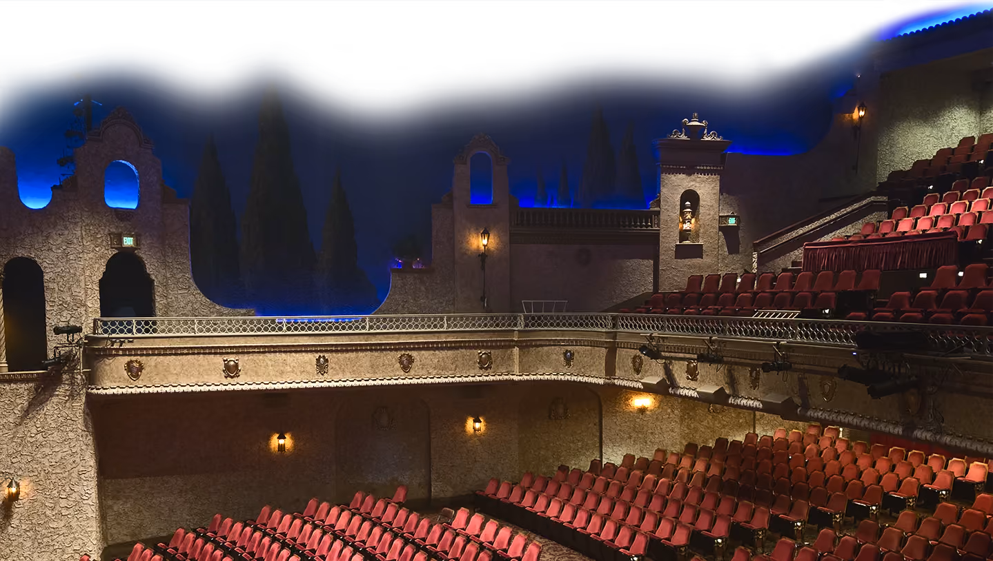 Empty theater auditorium with red seats and decorative beige walls under blue ambient lighting.
