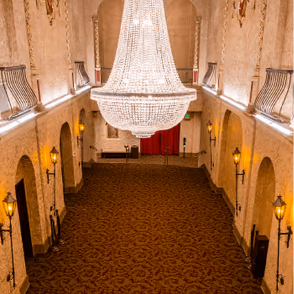 Lobby with large ornate chandelier, arched doorways, wall sconces, and patterned carpet.