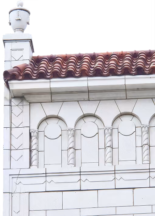 Detailed section of a building with ornate white stonework and a red wavy tile roof.