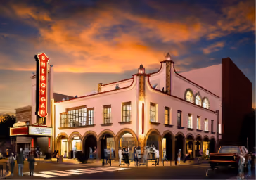 Historic movie theater building lit at dusk with marquee and arched windows on a vibrant sunset sky.