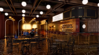 Dimly lit indoor rooftop patio with round tables, chairs, warm lighting, and a bar counter with a person behind it.