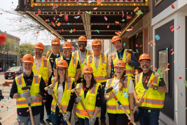 Group of construction workers in safety helmets and vests holding tools with confetti falling around.