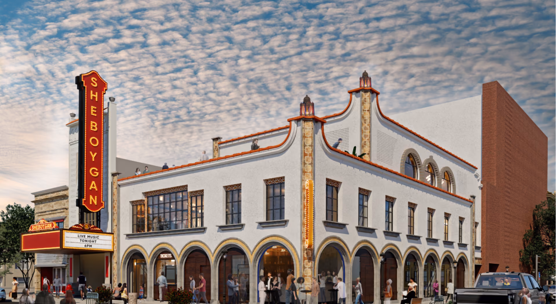 Crowded street view of Sheboygan theater with arched windows and people outside under a cloudy sky.