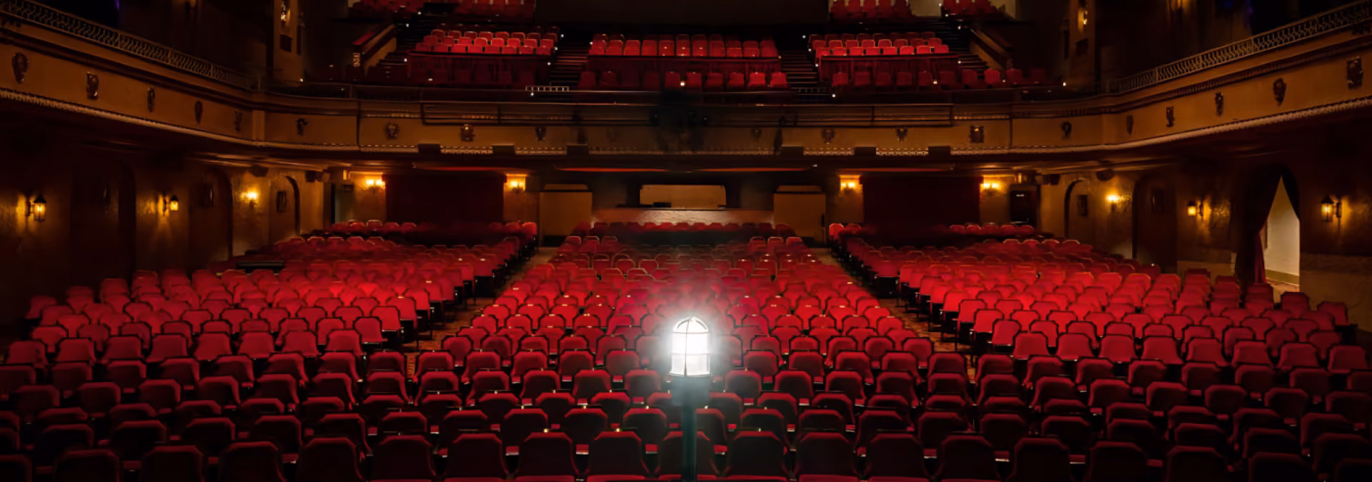 Empty theater with red seats and a bright light on a stand in the center aisle.