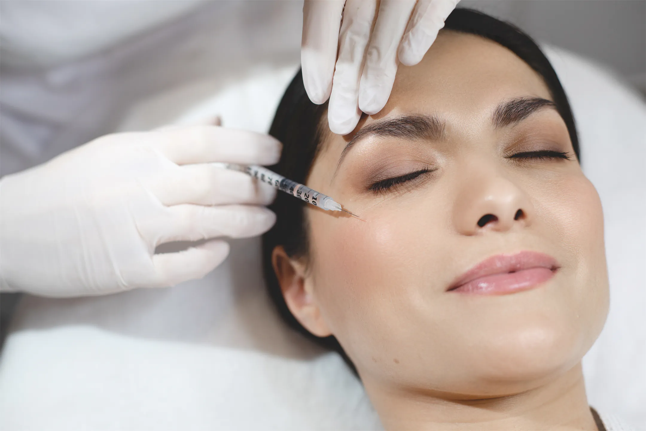 Provider injecting near the brow of a relaxed woman lying on a treatment bed