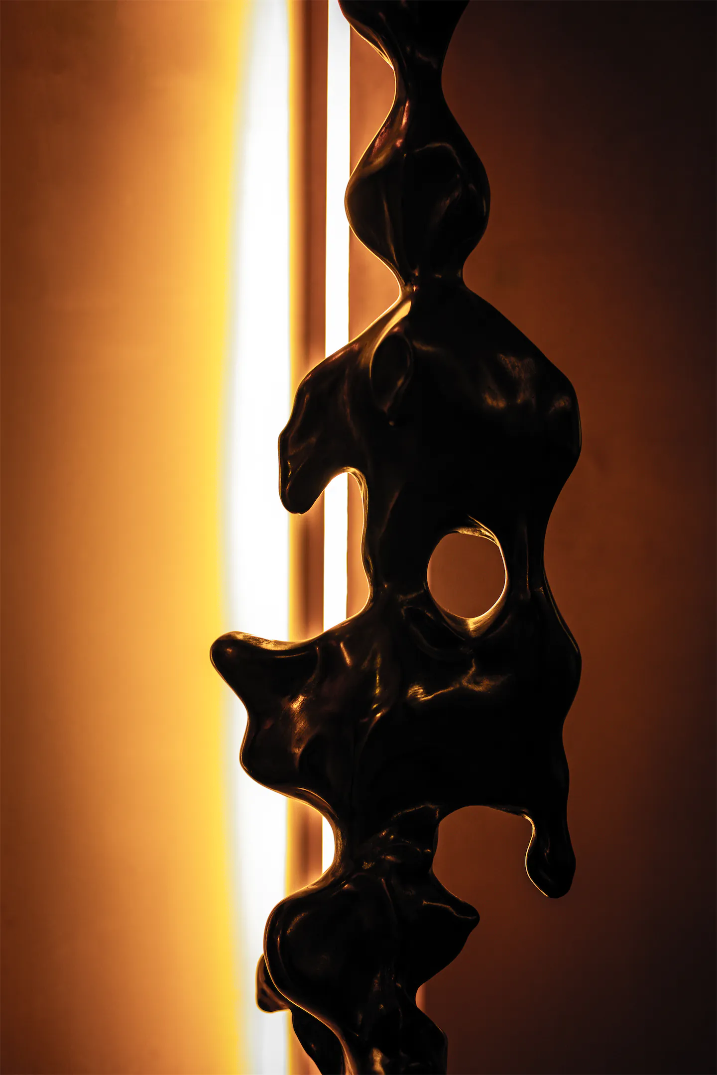 Dark sculptural art piece silhouetted against warm amber light