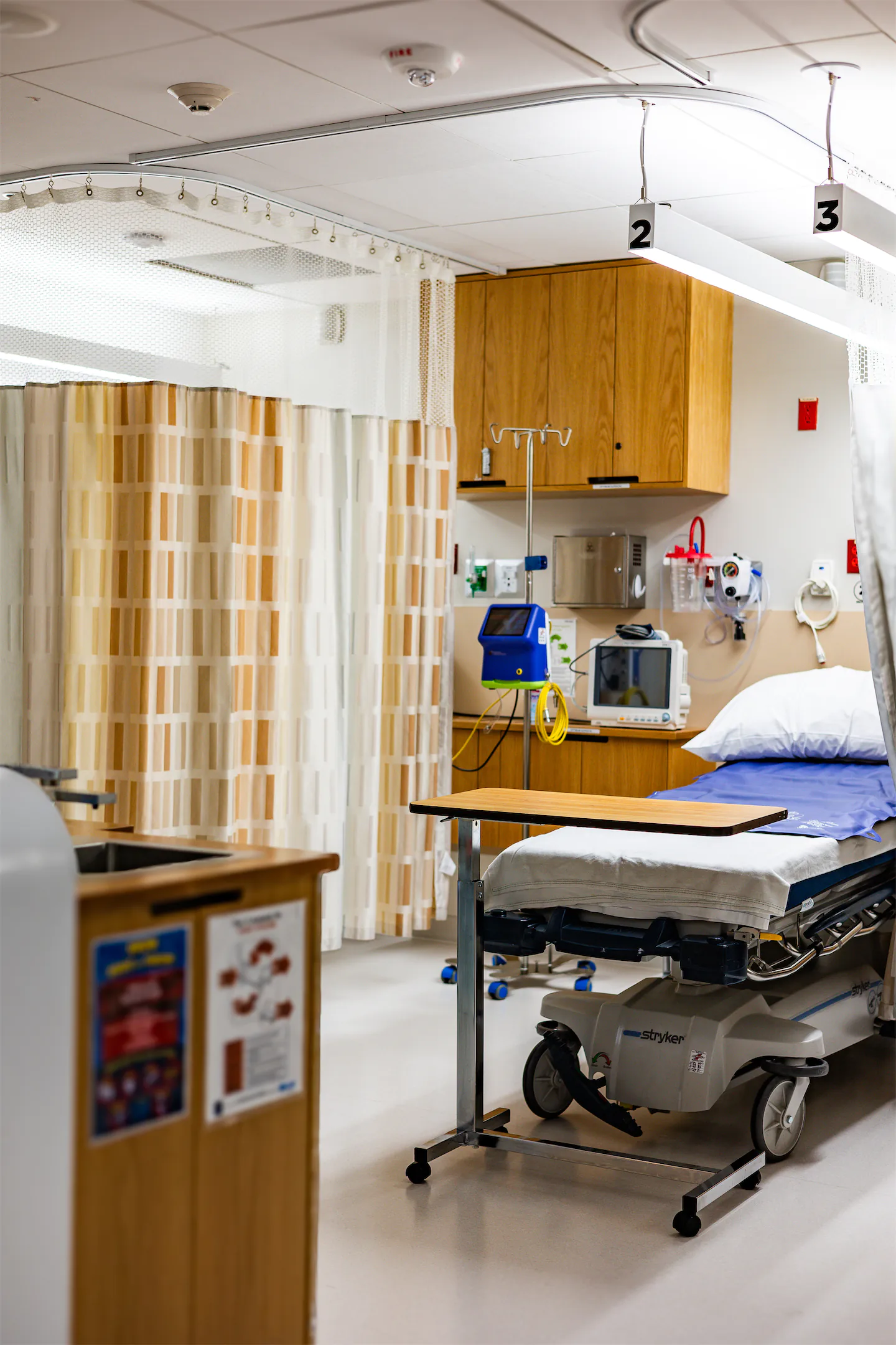 Hospital-style recovery bay with a patient bed, privacy curtains, and monitoring equipment