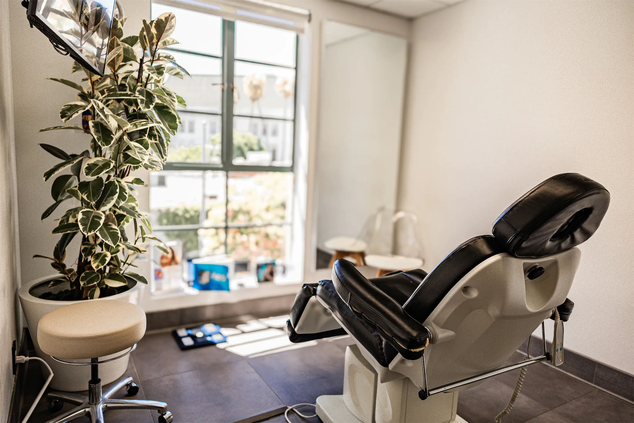 Sunlit treatment room with a reclining treatment chair beside a large window and plant