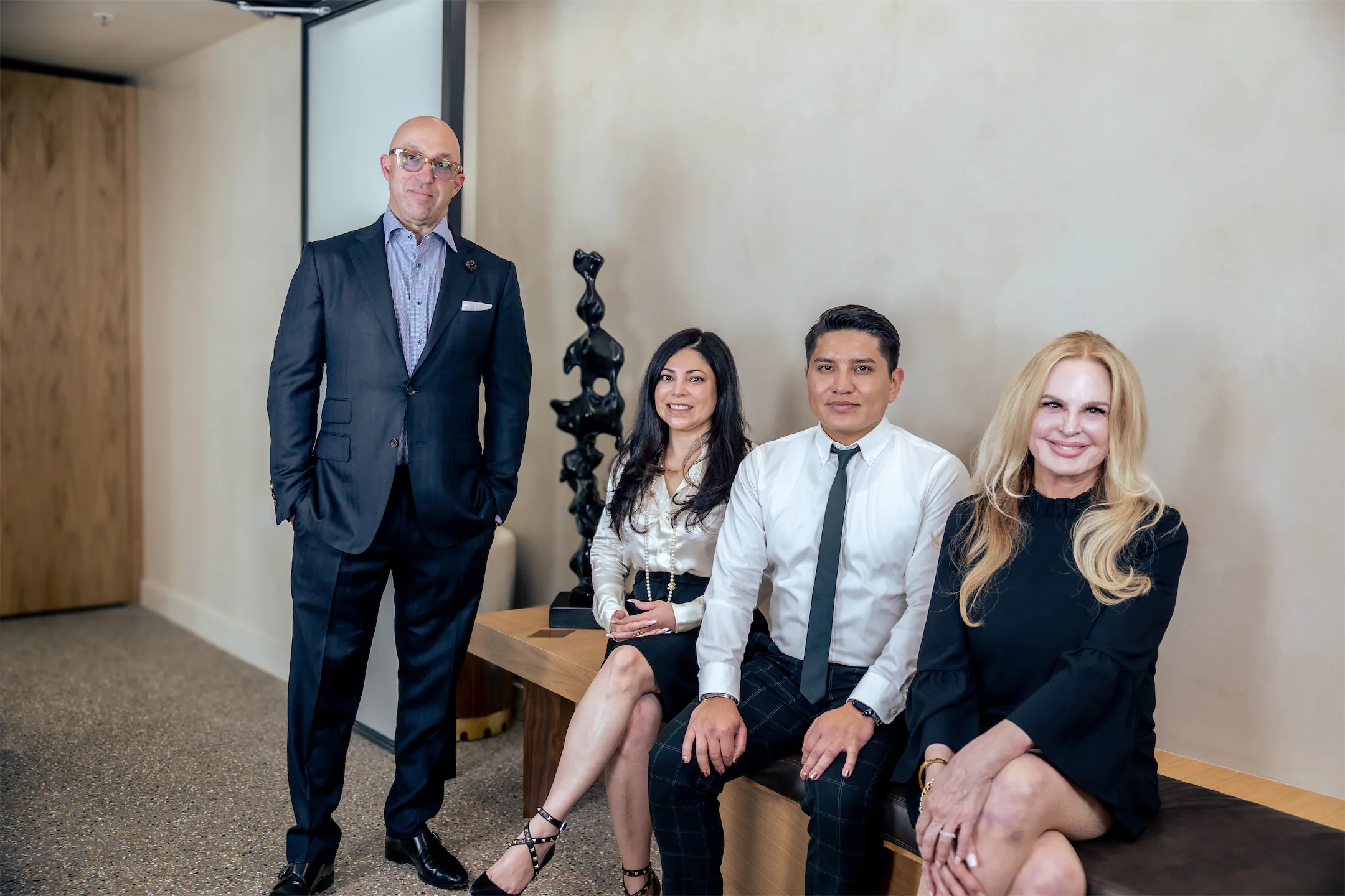 Four GVMD team members in the office, one standing beside three seated on a bench