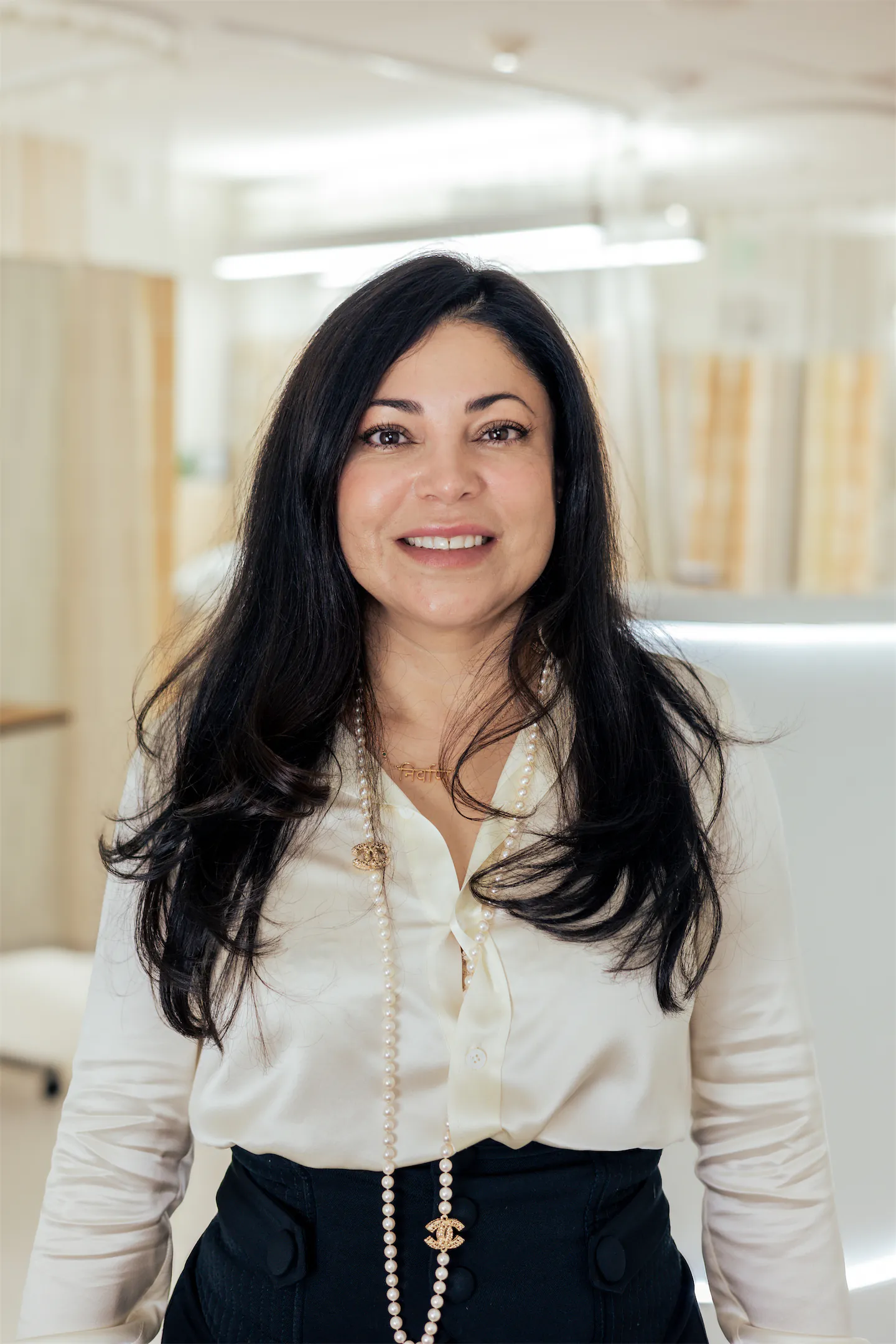Jessie Suarez smiling in a cream blouse and long pearl necklace in the GVMD office