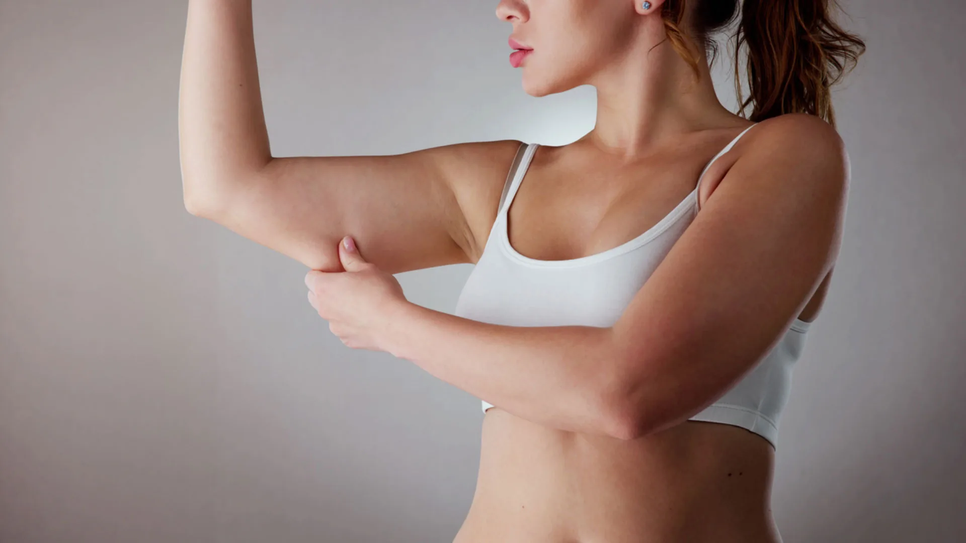 Woman in a sports bra pinching the skin of her raised upper arm