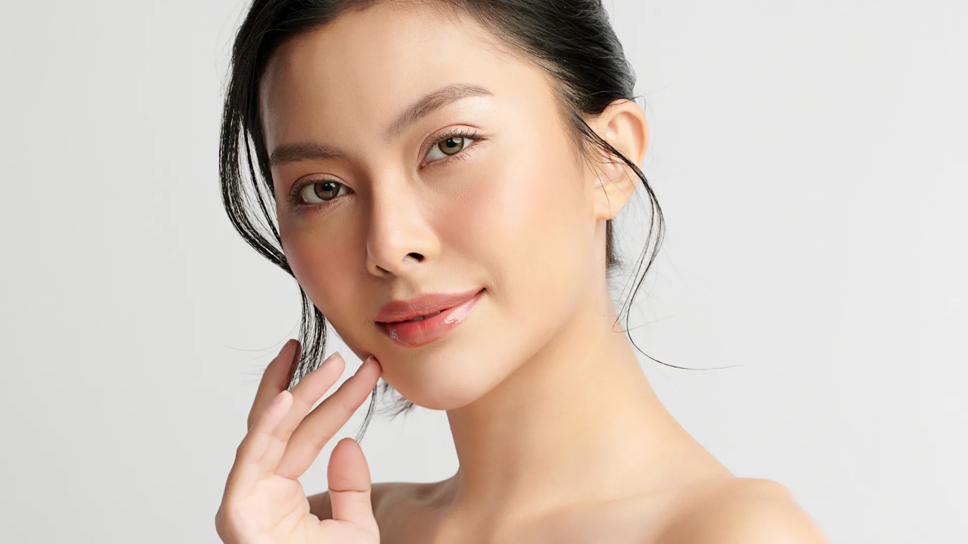 Smiling woman with her hair pulled back touching her jaw, looking at the camera
